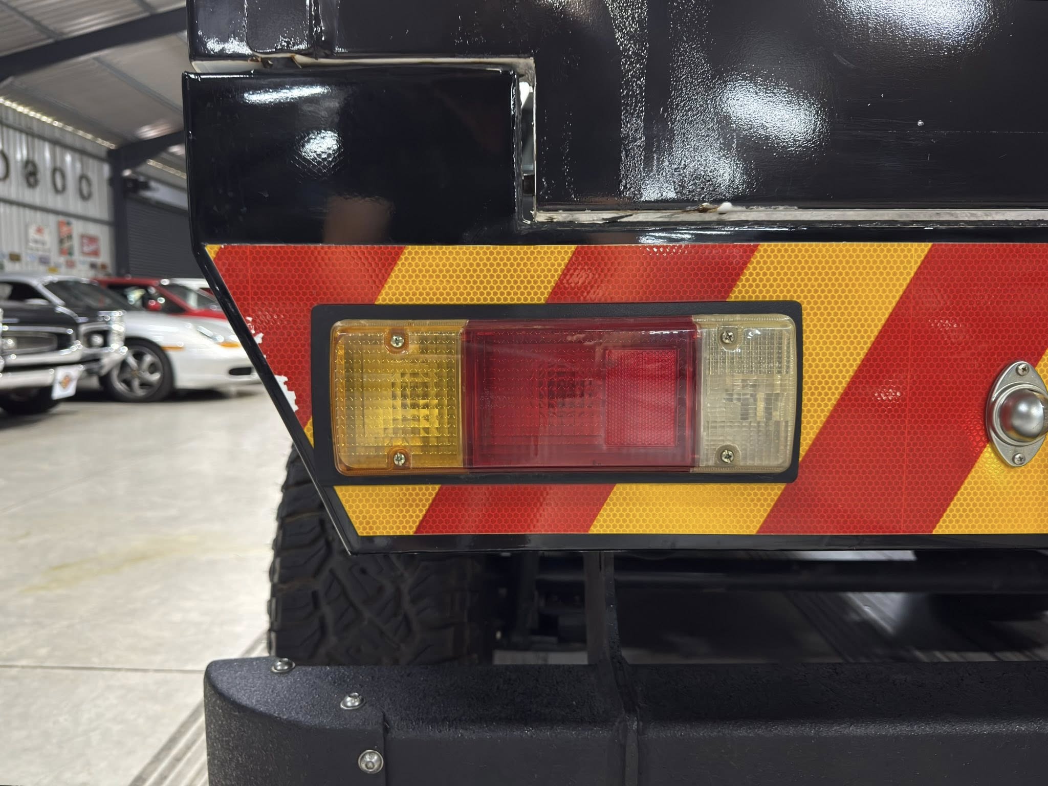 Rear of a black vehicle with red-and-yellow chevron reflective safety tape and taillight in a workshop setting.