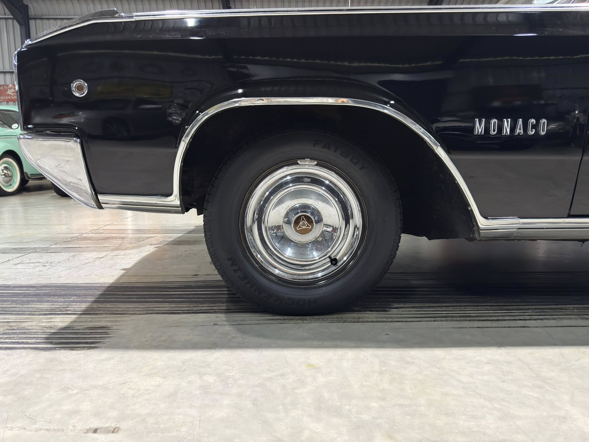 Close-up of a glossy black vintage car showing chrome wheel arch trim, hubcap detail, and the 'MONACO' lettering on the body.