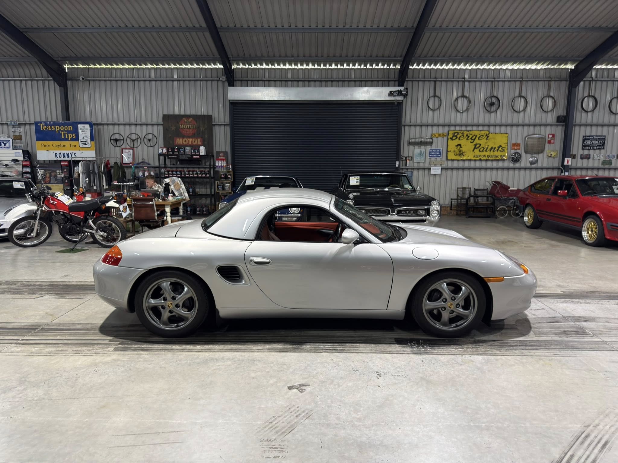 Silver Porsche convertibile in a vintage car showroom, with motorcycles and retro signs in the background