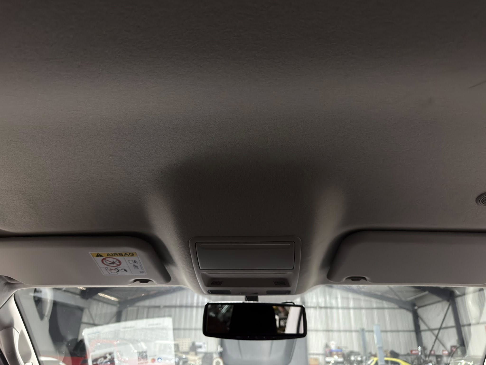 Interior of a car ceiling showing sun visors, overhead console, and rearview mirror reflected in the windshield.