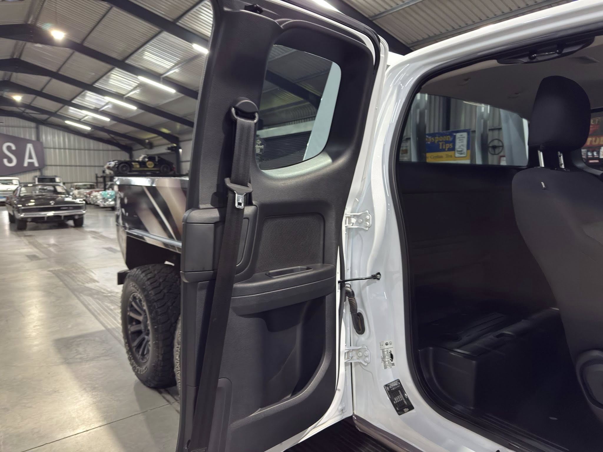 Open white SUV door showing interior black seats in a showroom with vintage cars in the background