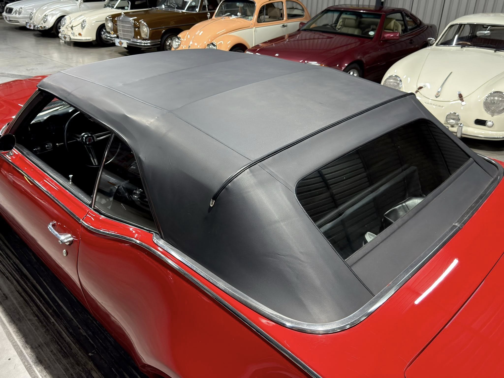 Close-up of a red convertible with a gray soft top in a showroom, classic cars lined up in the background.