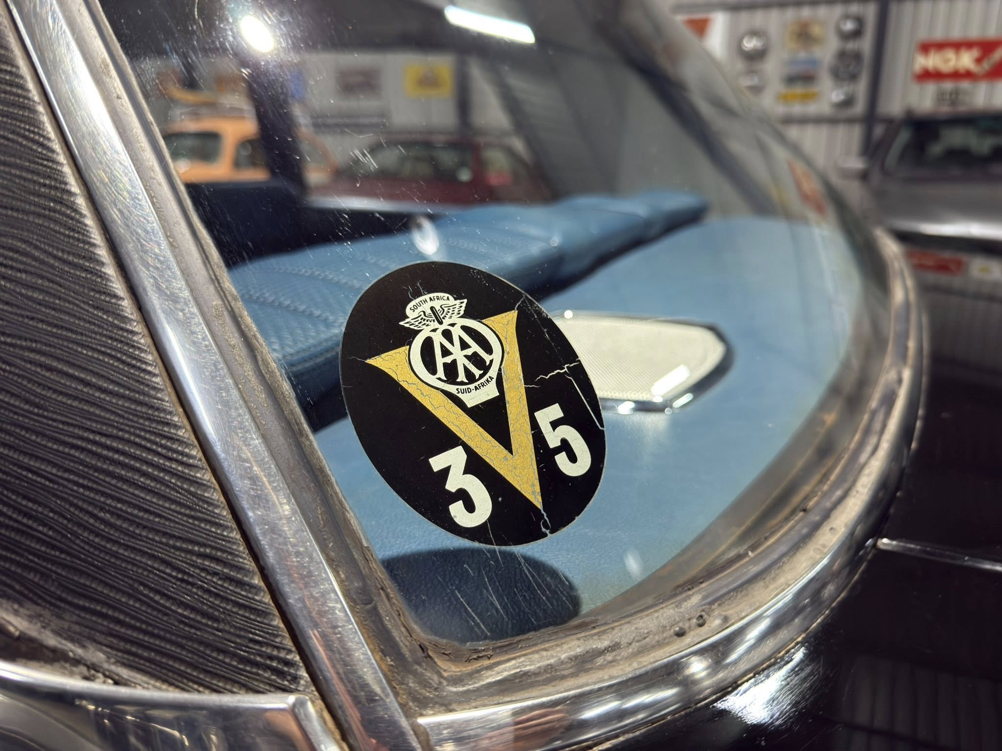 Close-up of a round black sticker on a vintage car windshield with a yellow triangle and the text 'South Africa' and 'Suid-Afrika' visible.