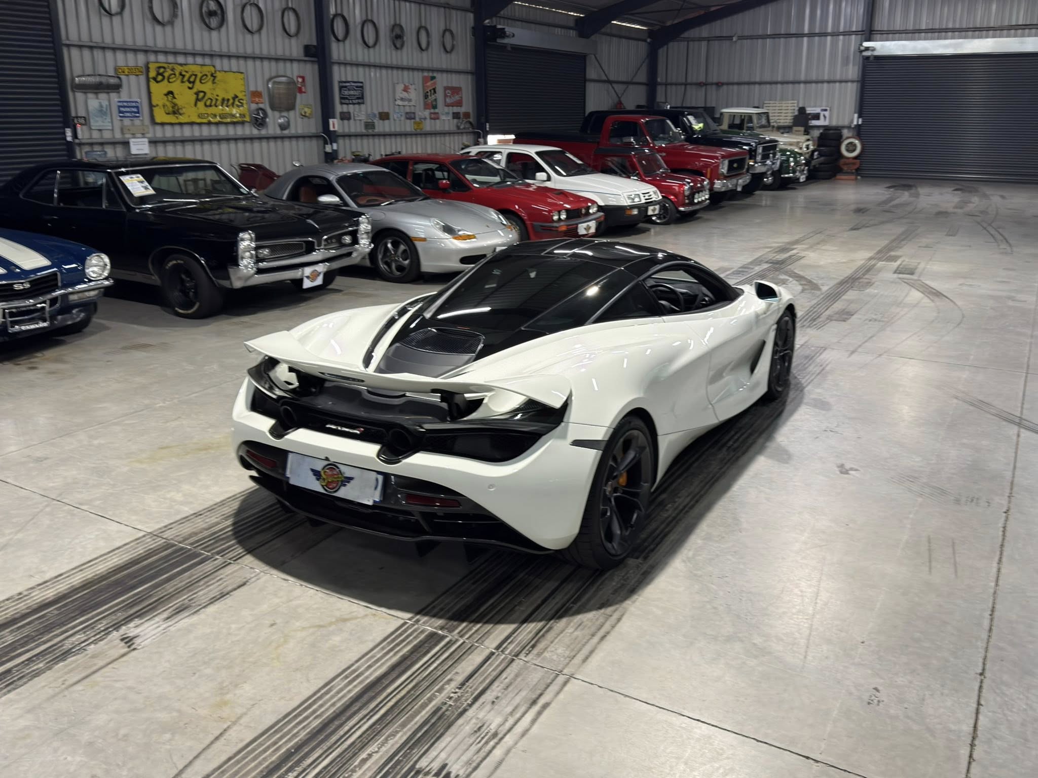 Indoor showroom/garage with a long row of classic and modern cars parked along a wall with signs and tires as decor.