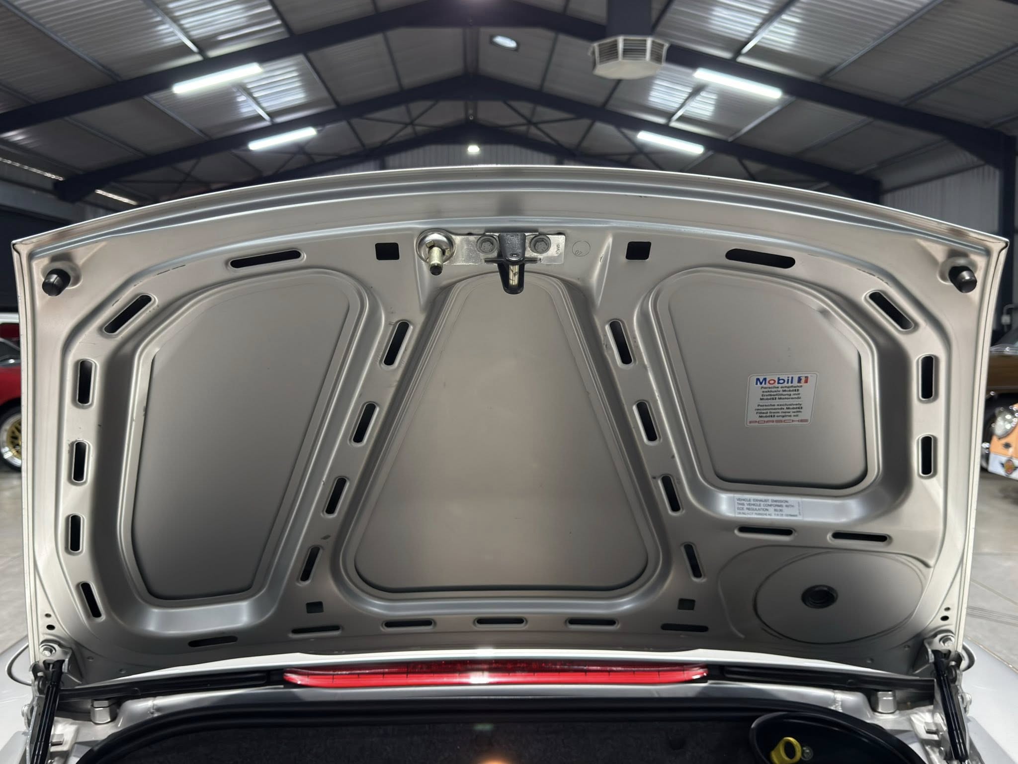 Open hatch of a silver car showing the trunk interior in a garage with metal beams and bright overhead lights