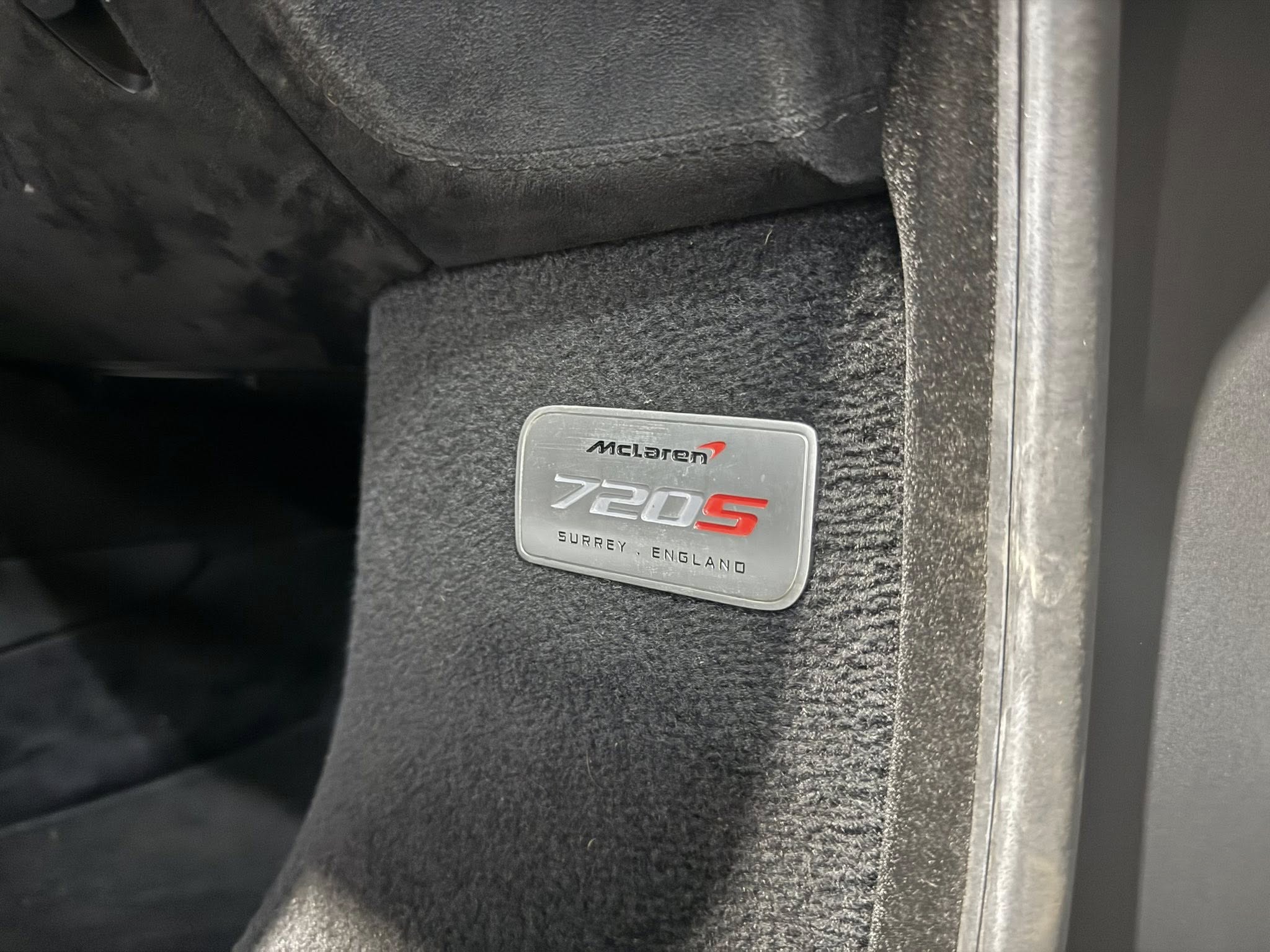 Close-up of a McLaren badge reading 720S on a black textured dashboard panel inside the car, Surrey England.