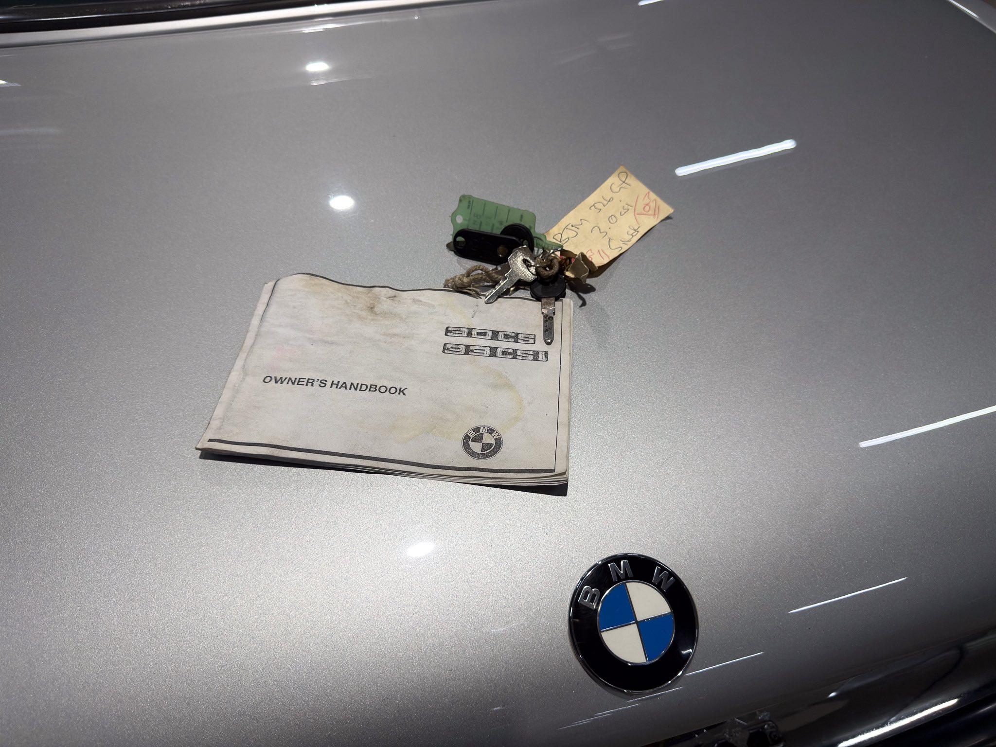 BMW car hood with key ring and owner's manual on a silver surface, BMW emblem visible