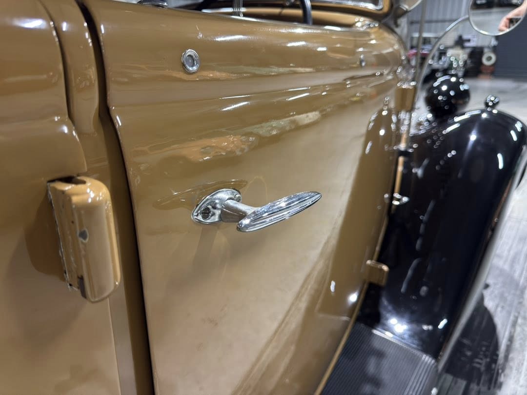 Chrome door handle on a brown vintage car door, close-up detail in a showroom setting.