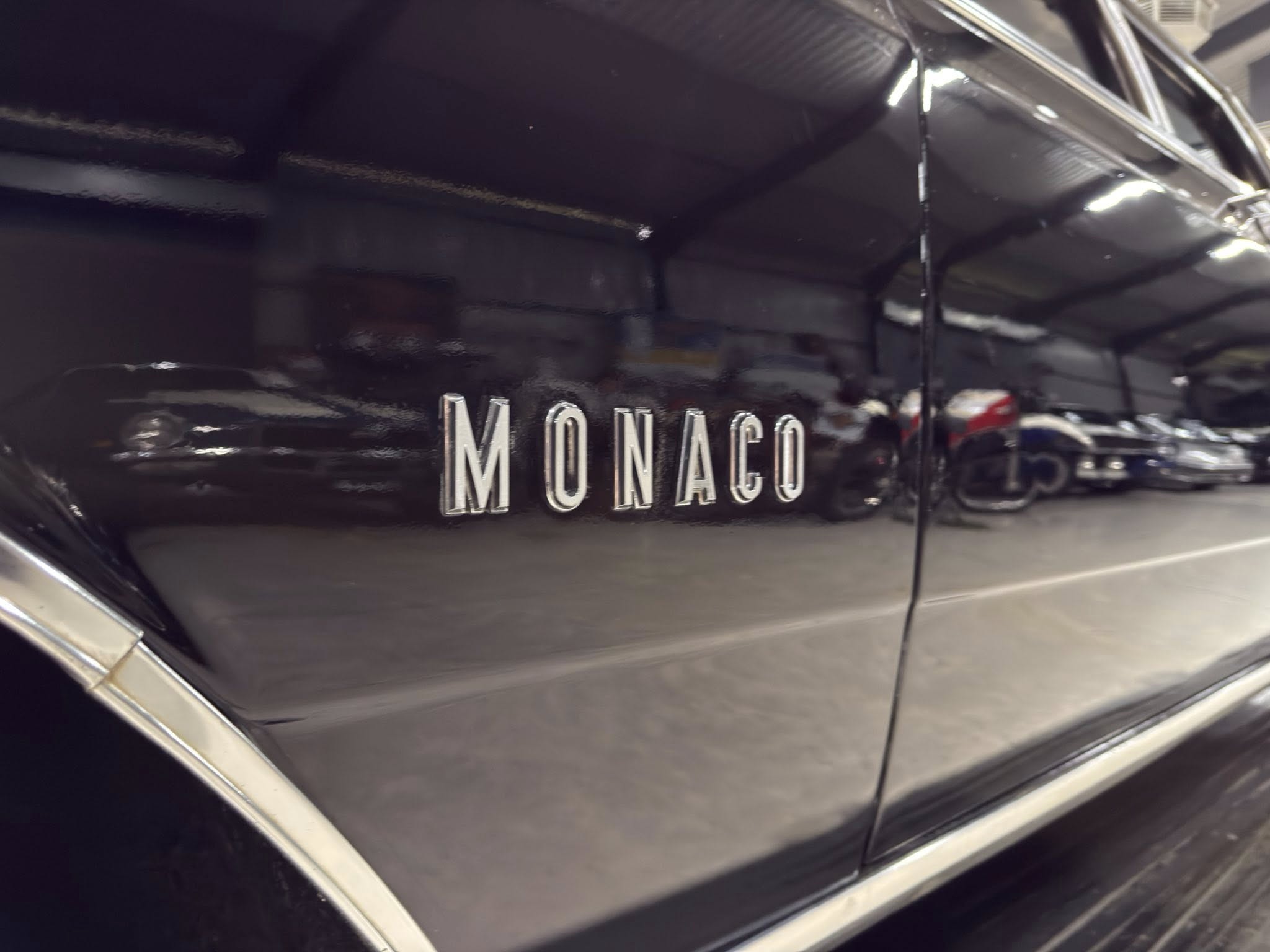 Close-up of chrome 'MONACO' badge on a glossy black car body with reflections.