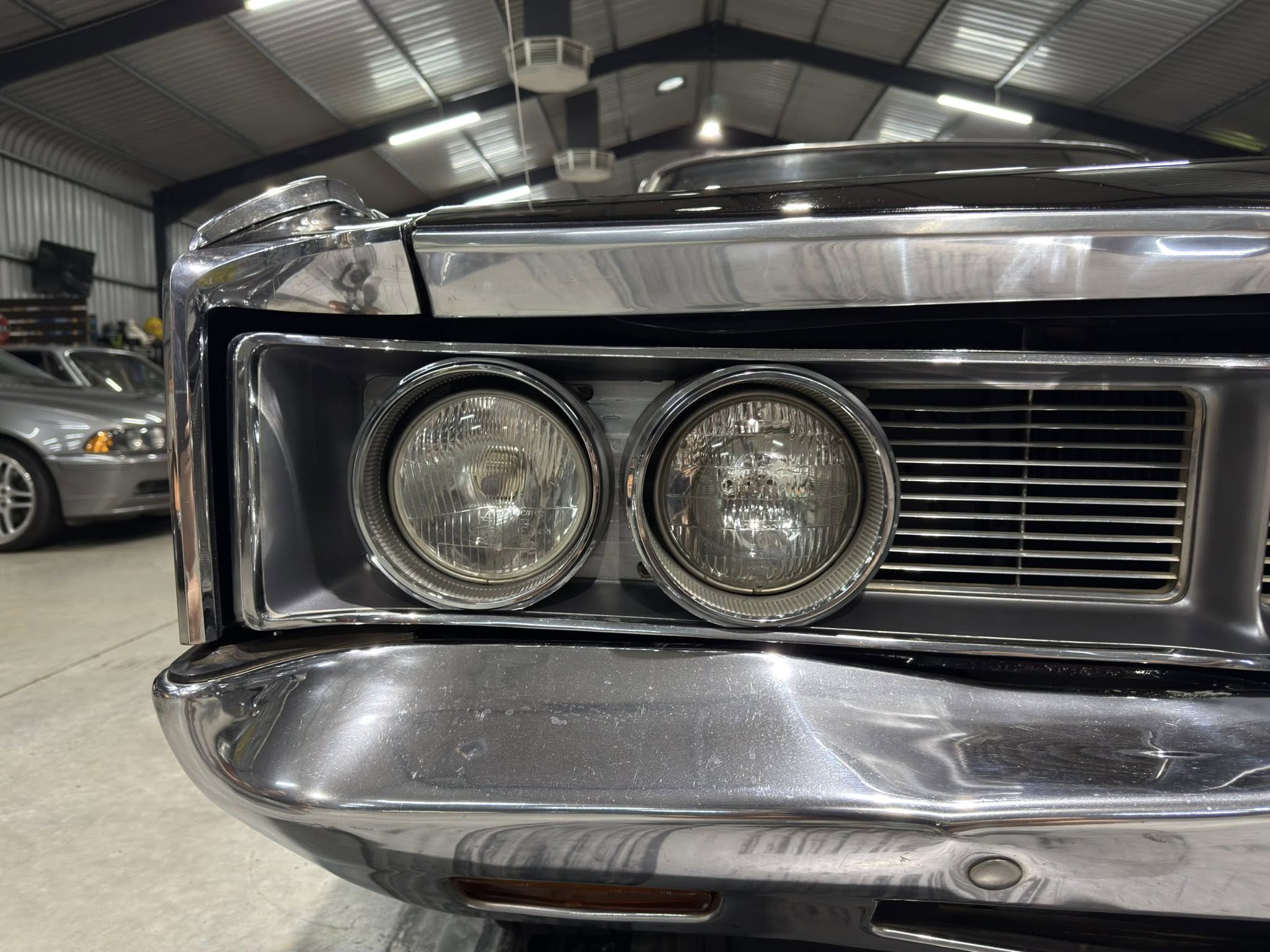 Close-up of a chrome car front end with dual round headlights in a showroom or garage setting.