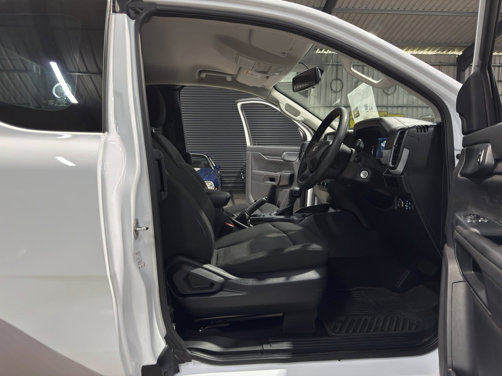 Open driver-side door of a white pickup showing the front seats, steering wheel, and dashboard in a garage interior