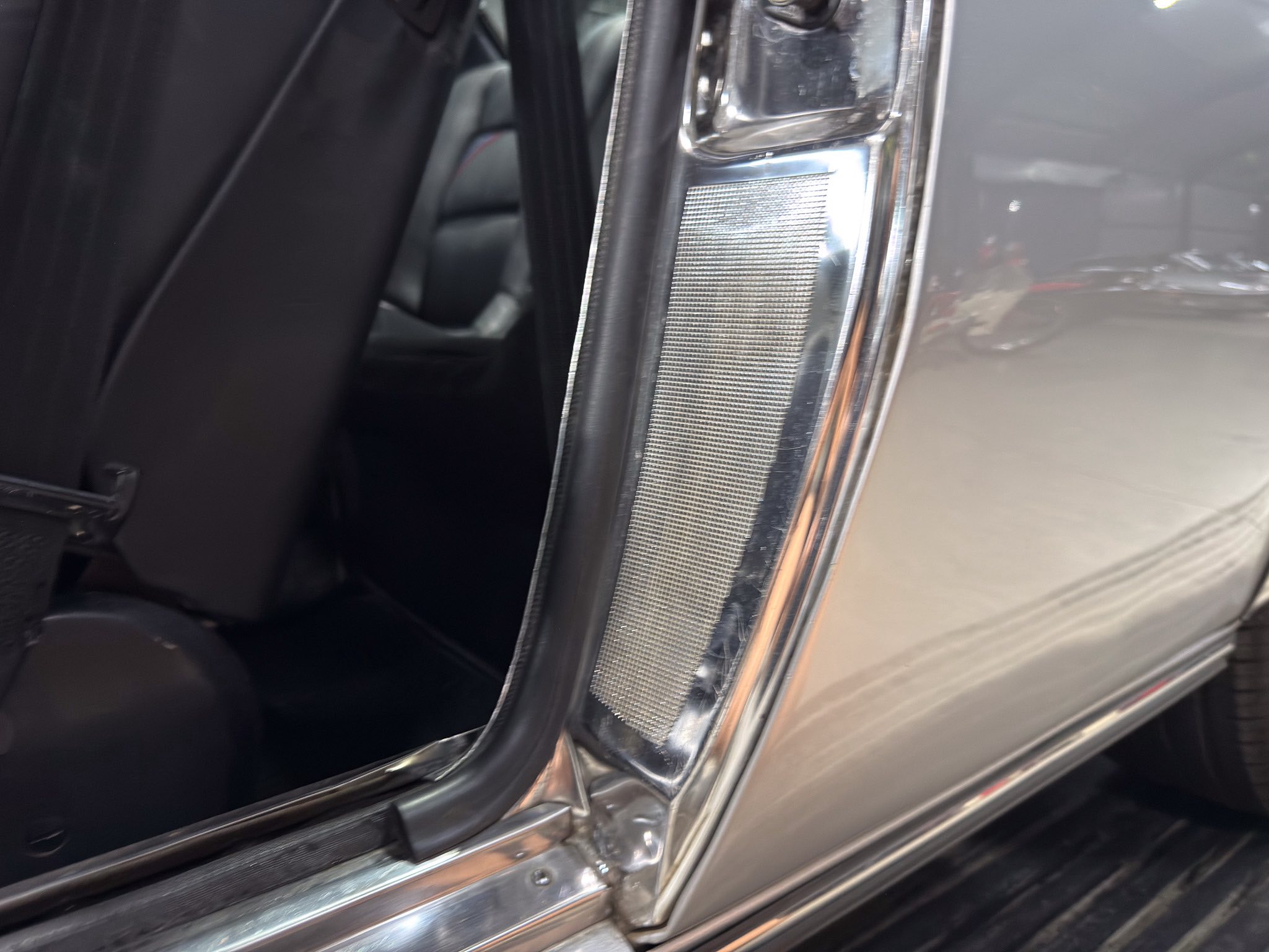 Close-up of a car door jamb showing chrome trim and a textured metal panel inside the frame.