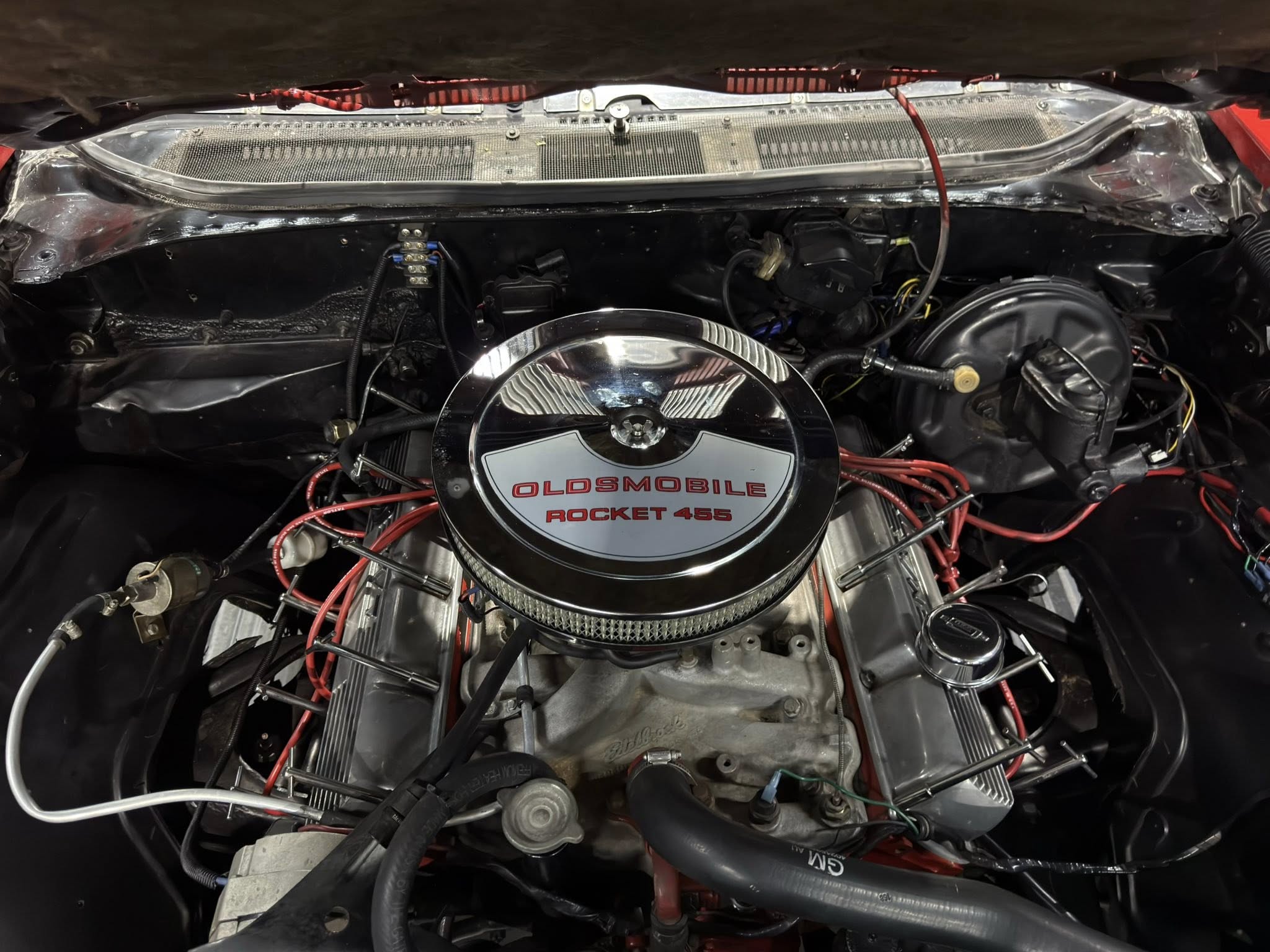 Under-hood view of a classic Oldsmobile Rocket 455 V8 engine with a chrome round air cleaner labeled 'Oldsmobile Rocket 455' at center, surrounded by hoses and wiring.