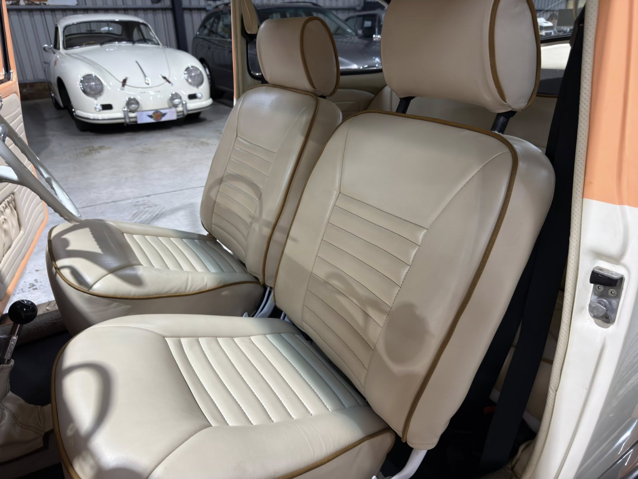 Beige leather car seats with brown piping inside a vintage car showroom; a white classic car is visible in the background.