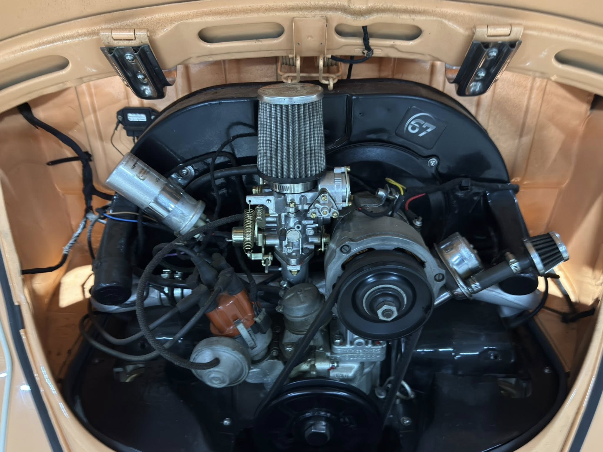 Open hood showing a vintage car engine with a large cone air filter, carburetor, and orange engine bay.