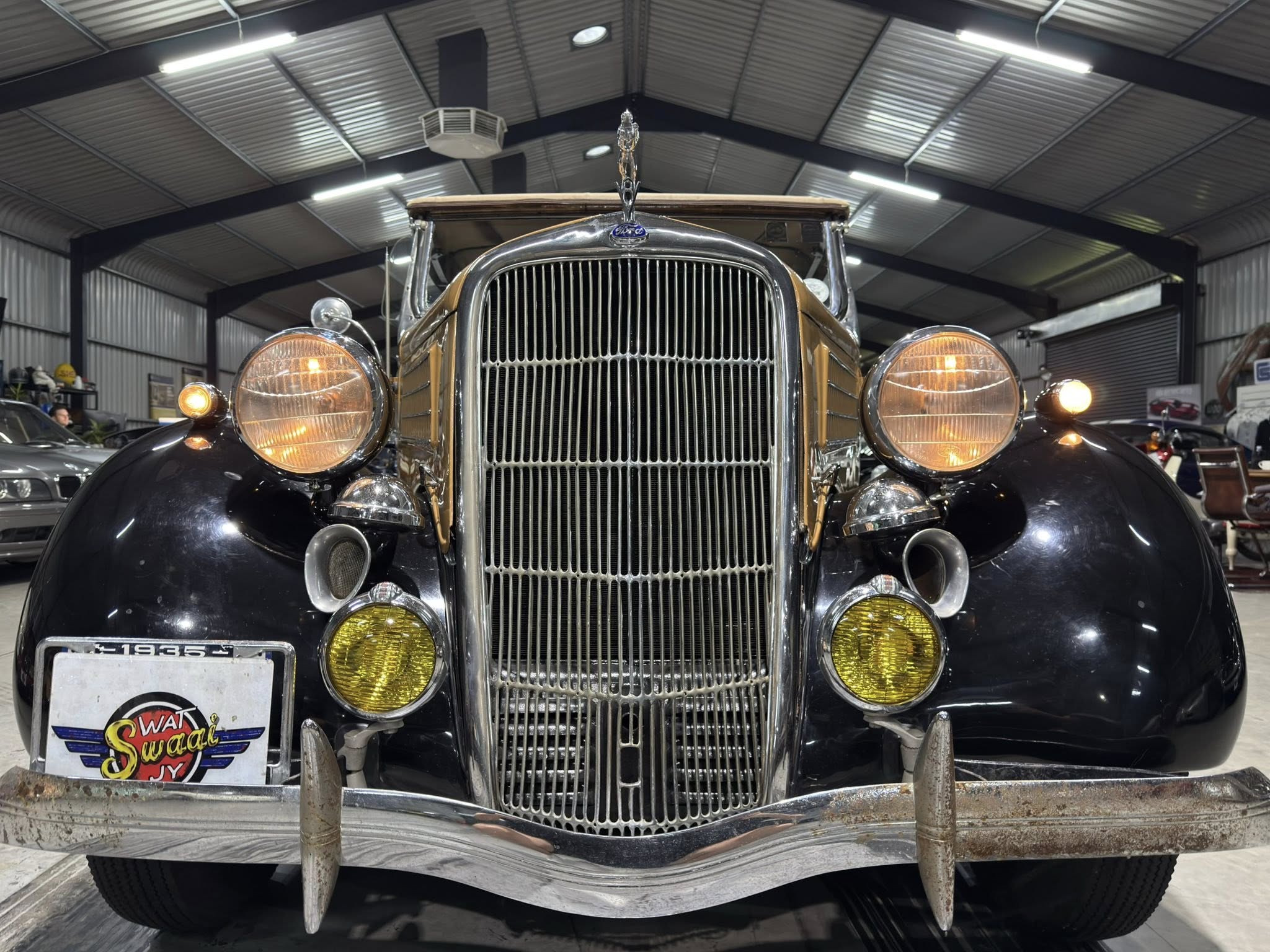 Front view of a vintage car with a tall chrome grille and round headlights in a well-lit showroom interior.