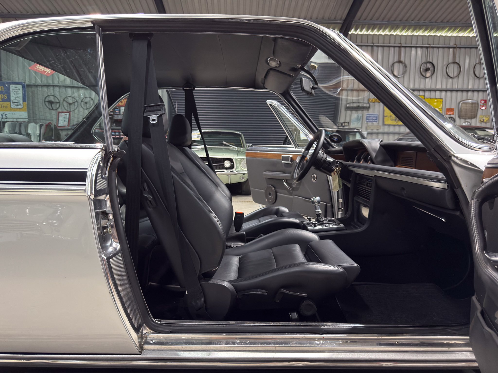 Interior of a gray vintage car with black leather seats, door open and steering wheel visible