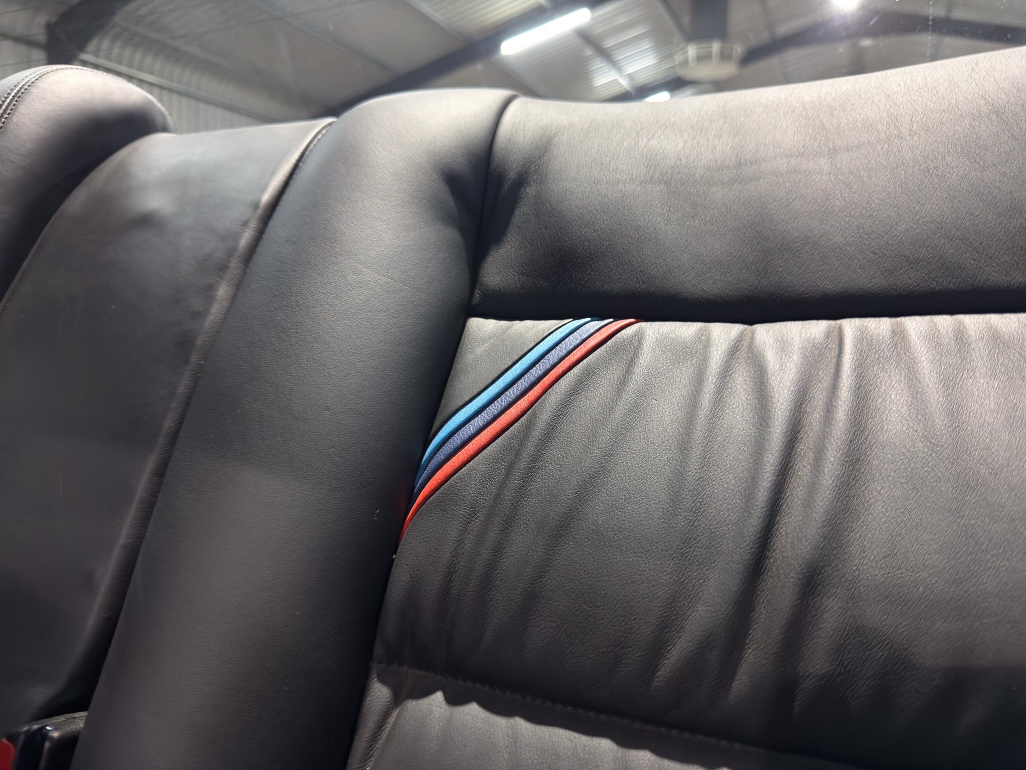 Close-up of black leather car seat with blue and red accent stitching/piping in the seam areas.