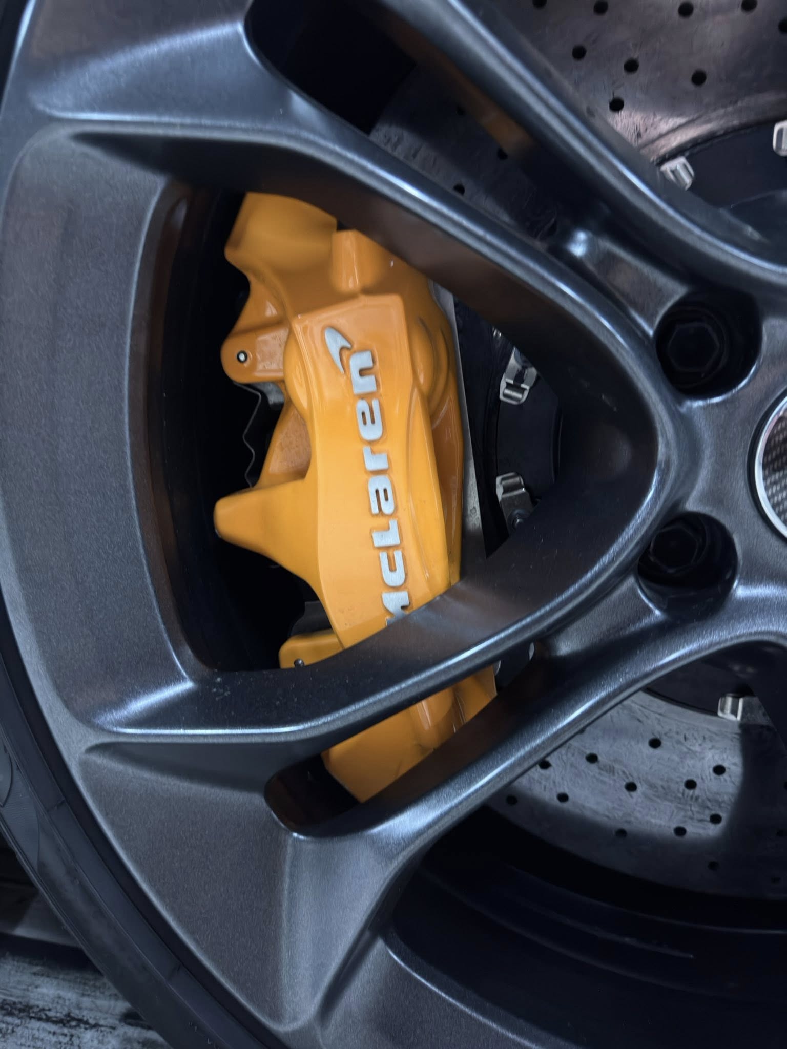 Orange brake caliper visible behind a dark alloy wheel, with a perforated rotor rest of the brake system behind it.