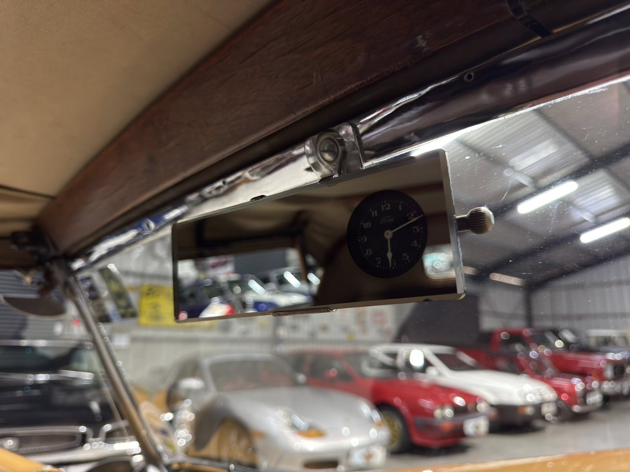 Close-up of a car dashboard clock and chrome frame inside a showroom, with blurred cars in the background.