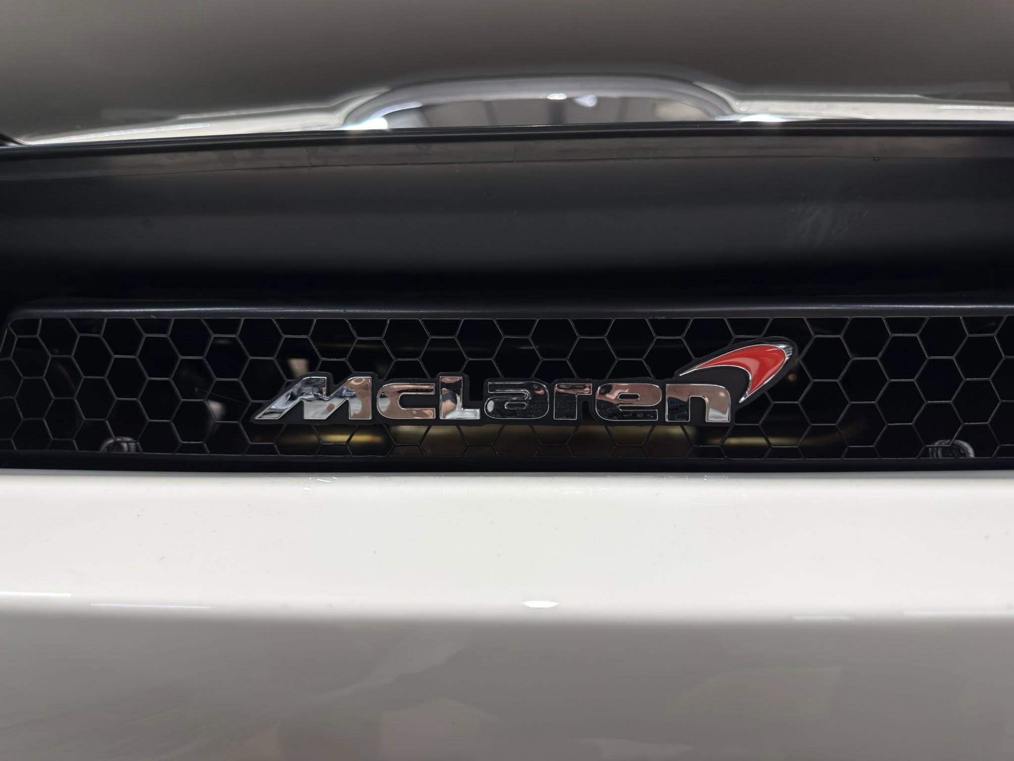 Front grille of a white McLaren car with a hexagonal mesh pattern and chrome badge visible on the right side