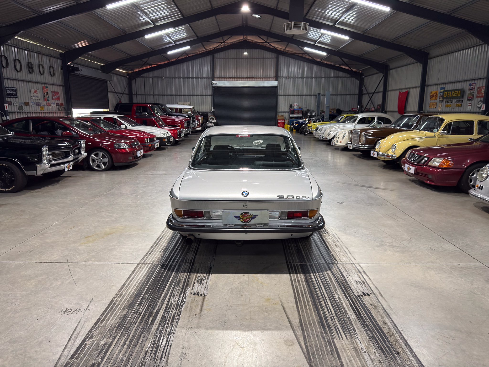 Indoor car showroom with a row of cars on both sides and a silver BMW in the foreground center.