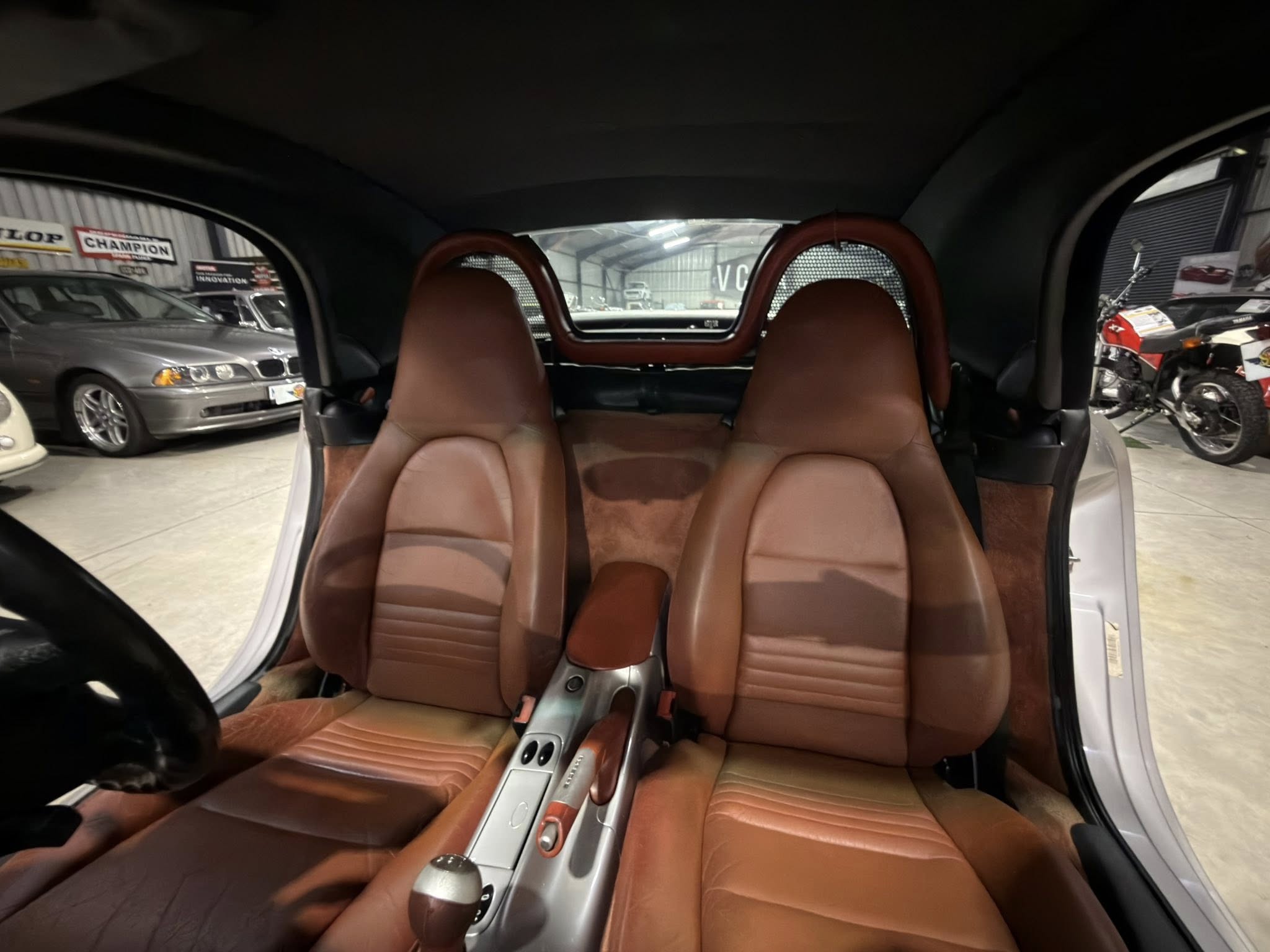 Back seat area of a car with tan/brown leather seats and a central console between the front seats; showroom floor and other vehicles visible outside the windows.