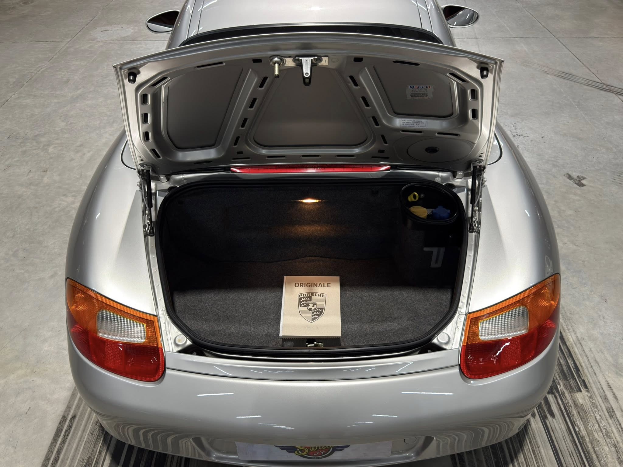 Open trunk of a silver Porsche with a brochure on the trunk floor showing the Porsche crest.