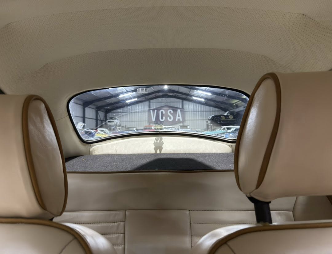 Rear interior of a beige-car, back seats visible, view through rear window to a hangar with 'VCSA' sign outside