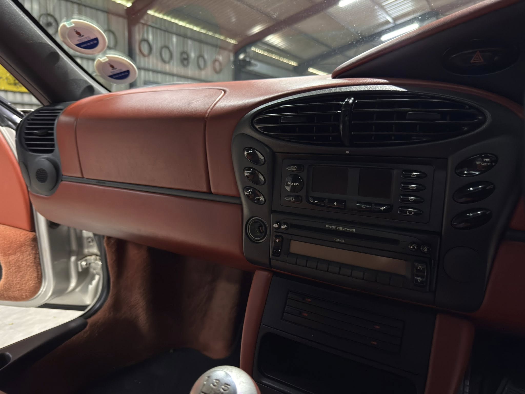 Brown leather car dashboard interior with central air vents, control panel, and a manual gear shifter visible in the foreground.