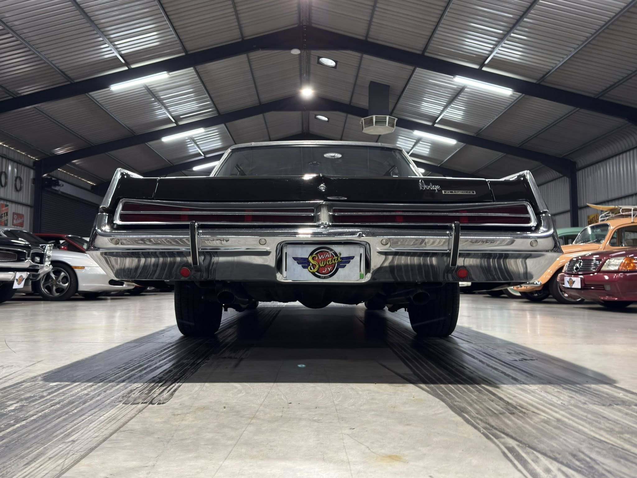 Rear view of a black vintage car in a showroom, with other classic cars and a metal ceiling above.