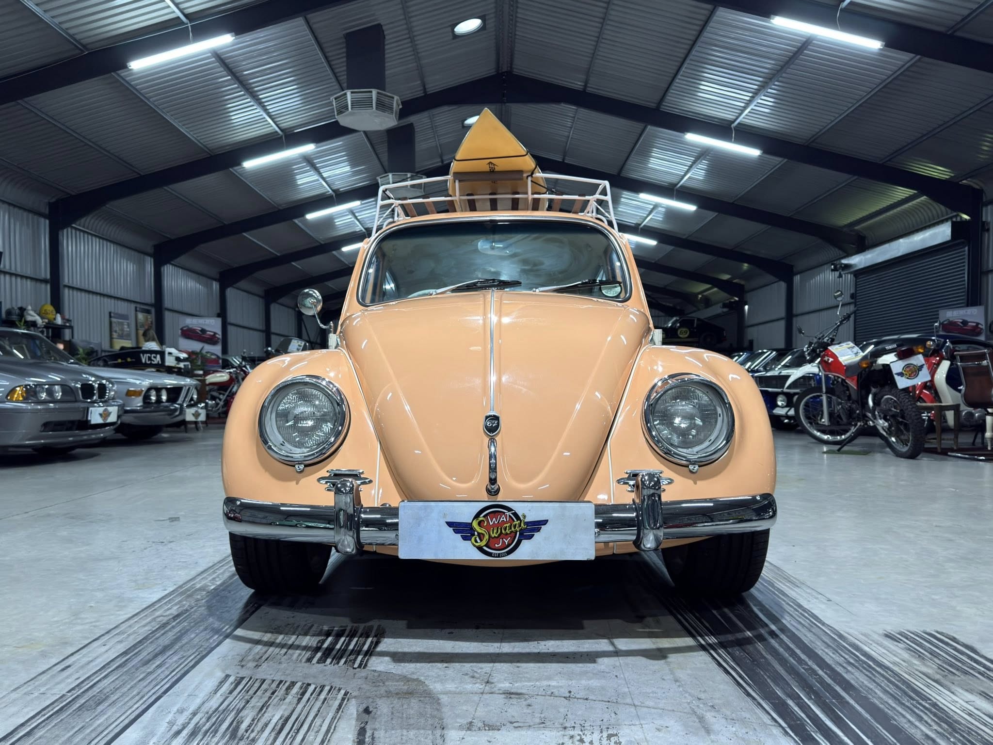 Front view of a peach-colored vintage car inside a showroom, with a yellow kayak secured on its roof rack.