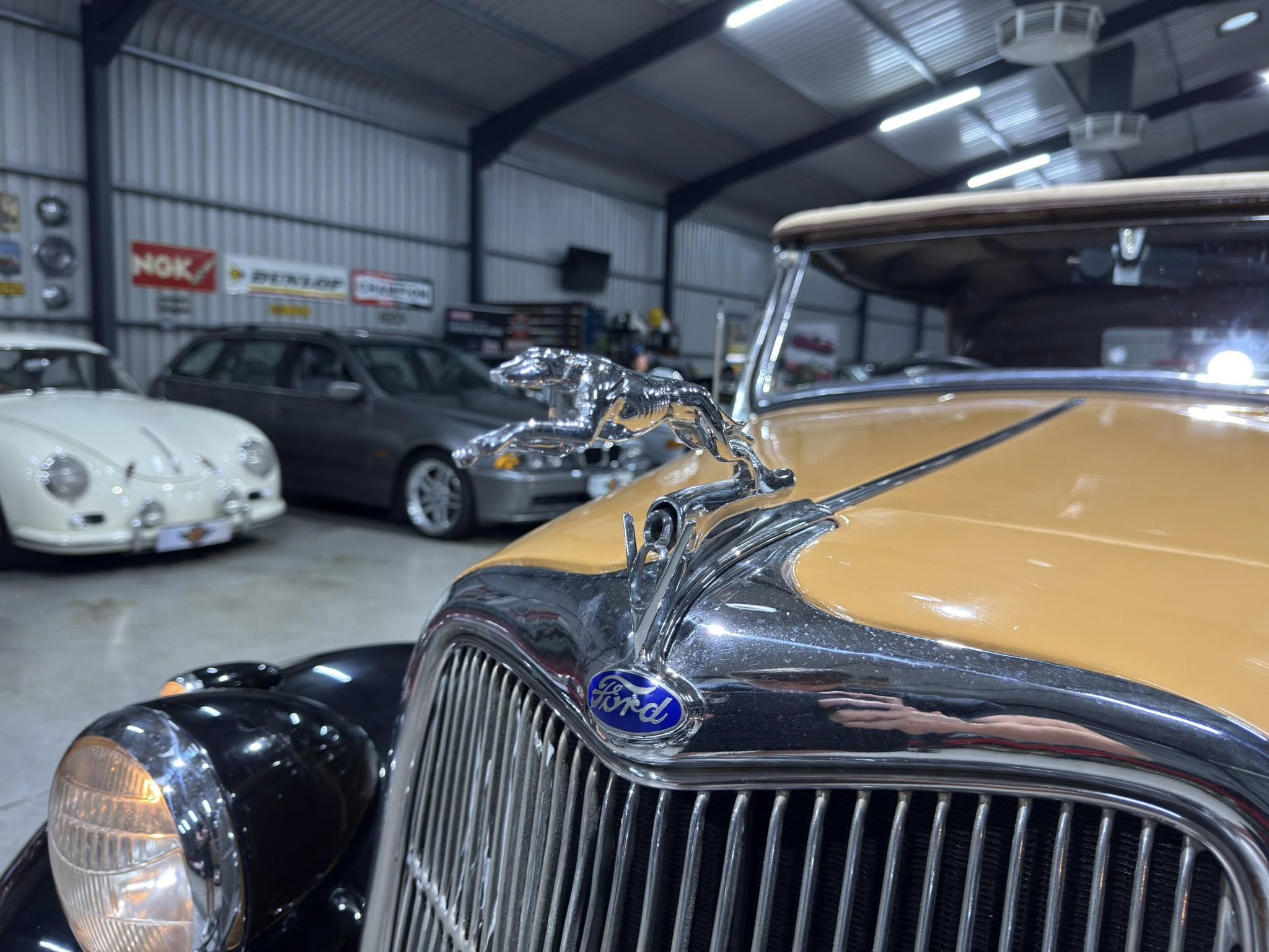 Close-up of a chrome hood ornament on a gold classic Ford in a car showroom workshop