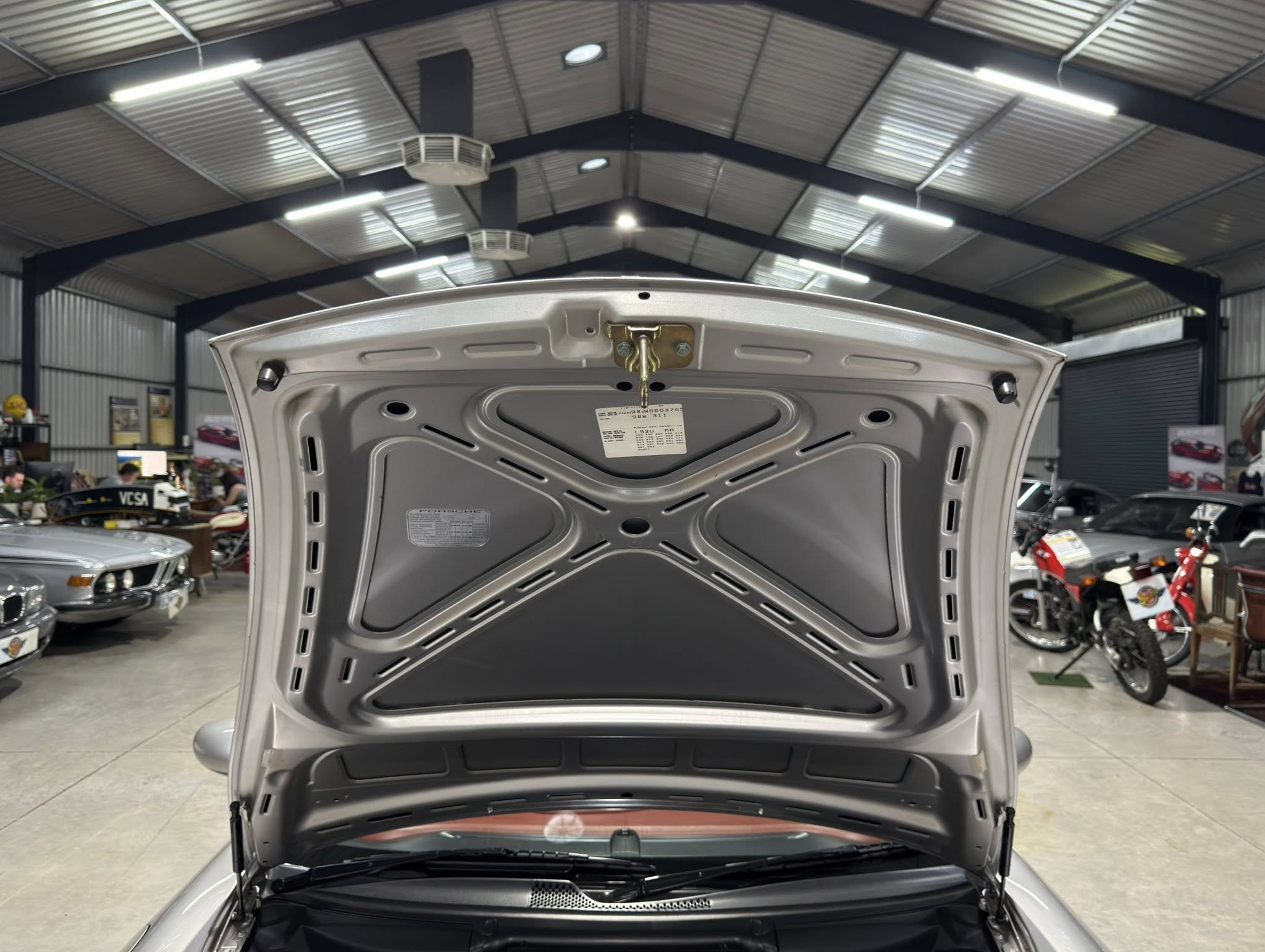 Open rear hatch of a silver SUV in a car showroom; overhead industrial ceiling and other vehicles in the background.