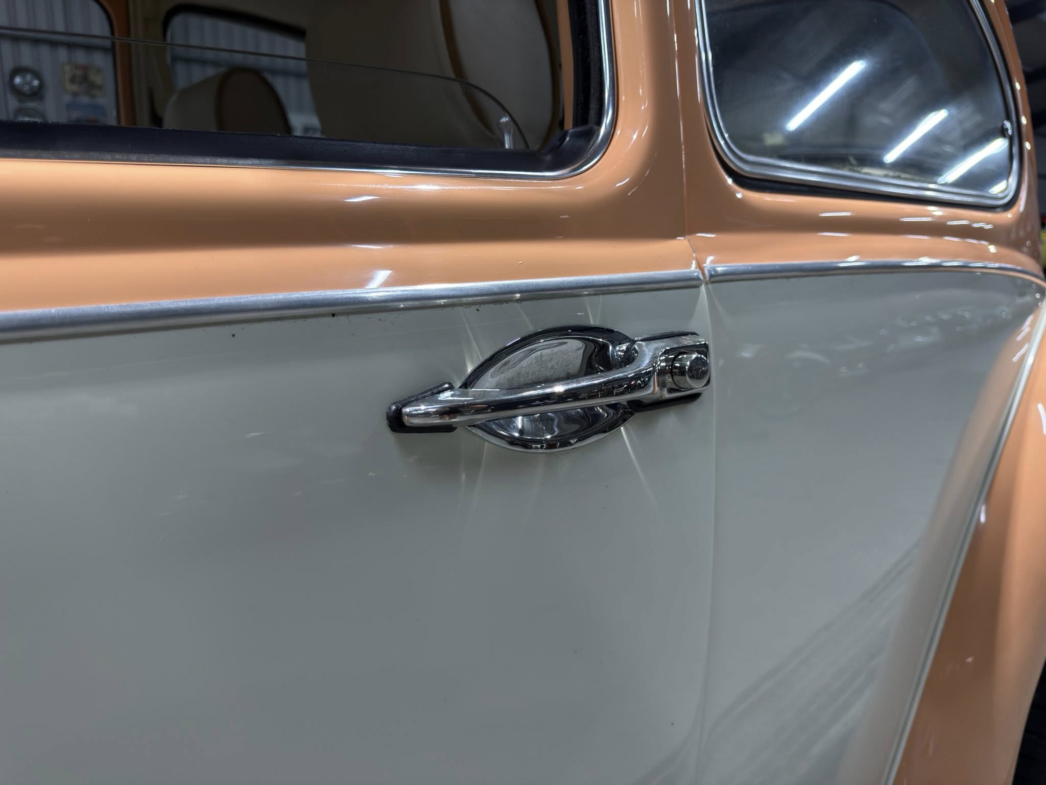 Close-up of a vintage car door with chrome handle and two-tone peach and gray paint