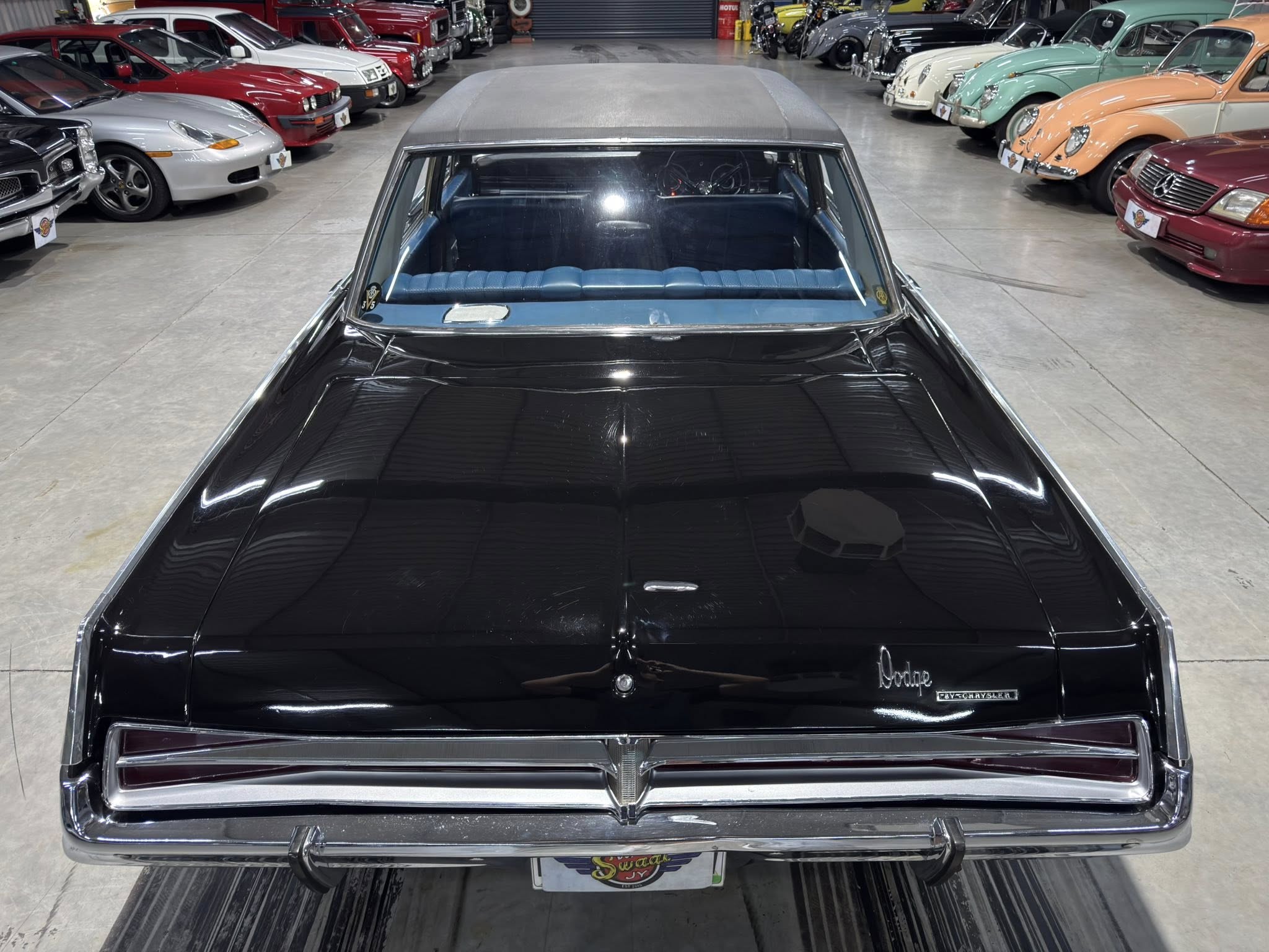 Rear view of a glossy black vintage Dodge in a showroom surrounded by colorful classic cars.