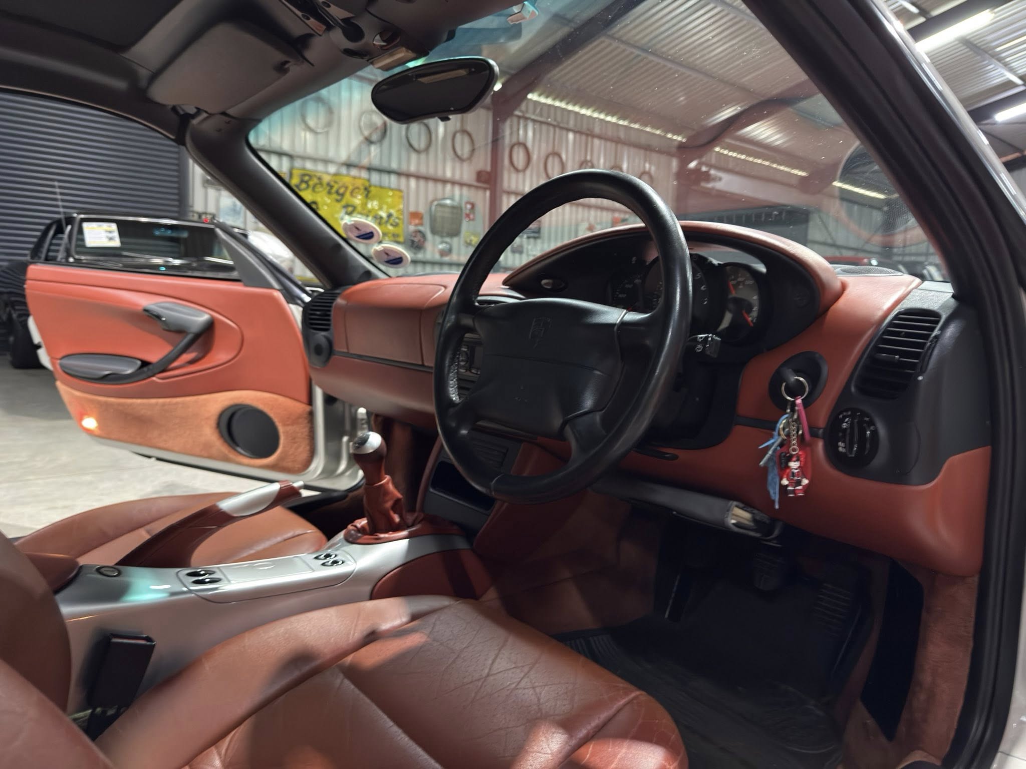 Interior of a red leather-upholstered car, showing the steering wheel, center console, and open door on the driver’s side in a garage or showroom setting.