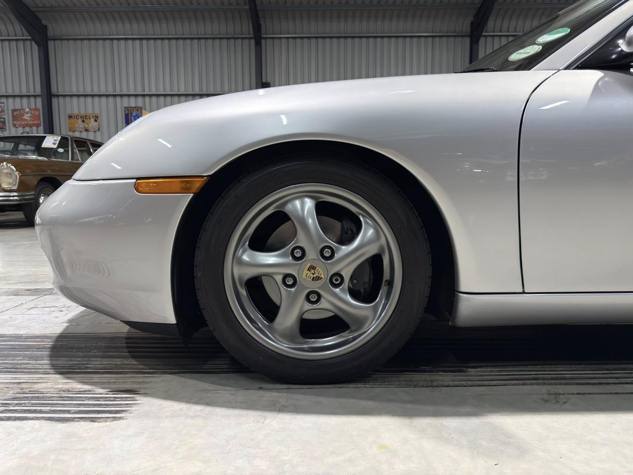 Close-up of a silver Porsche wheel and front fender in a showroom setting.