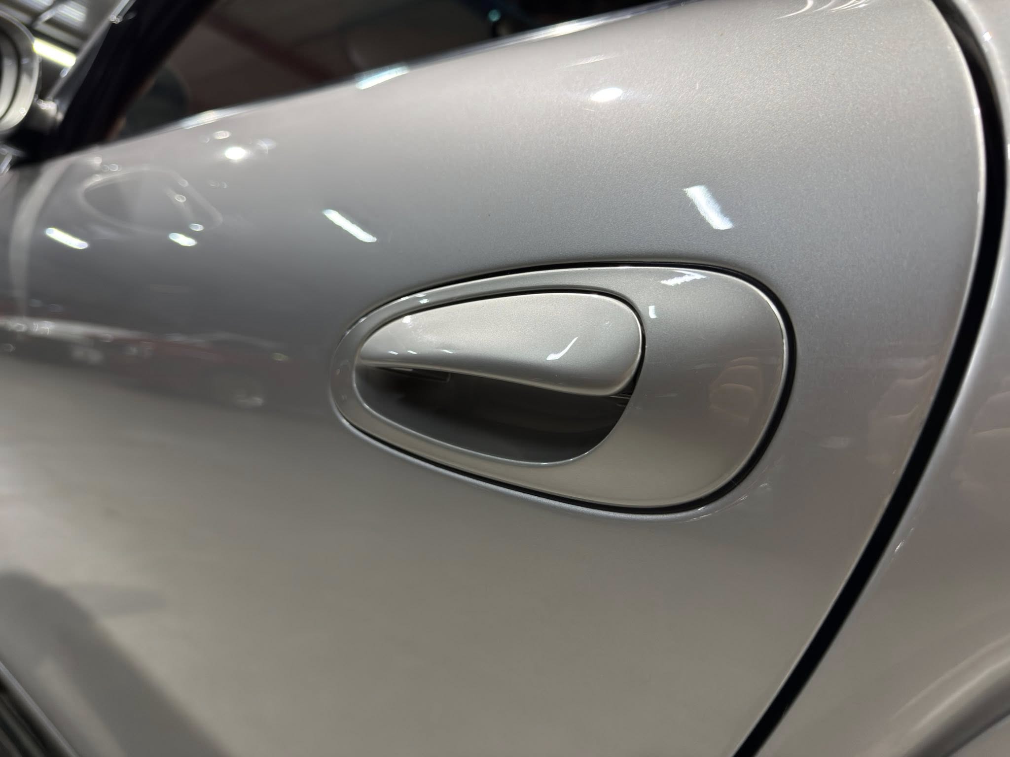 Close-up of a silver car door handle on a metallic gray vehicle, with reflections on the surface.