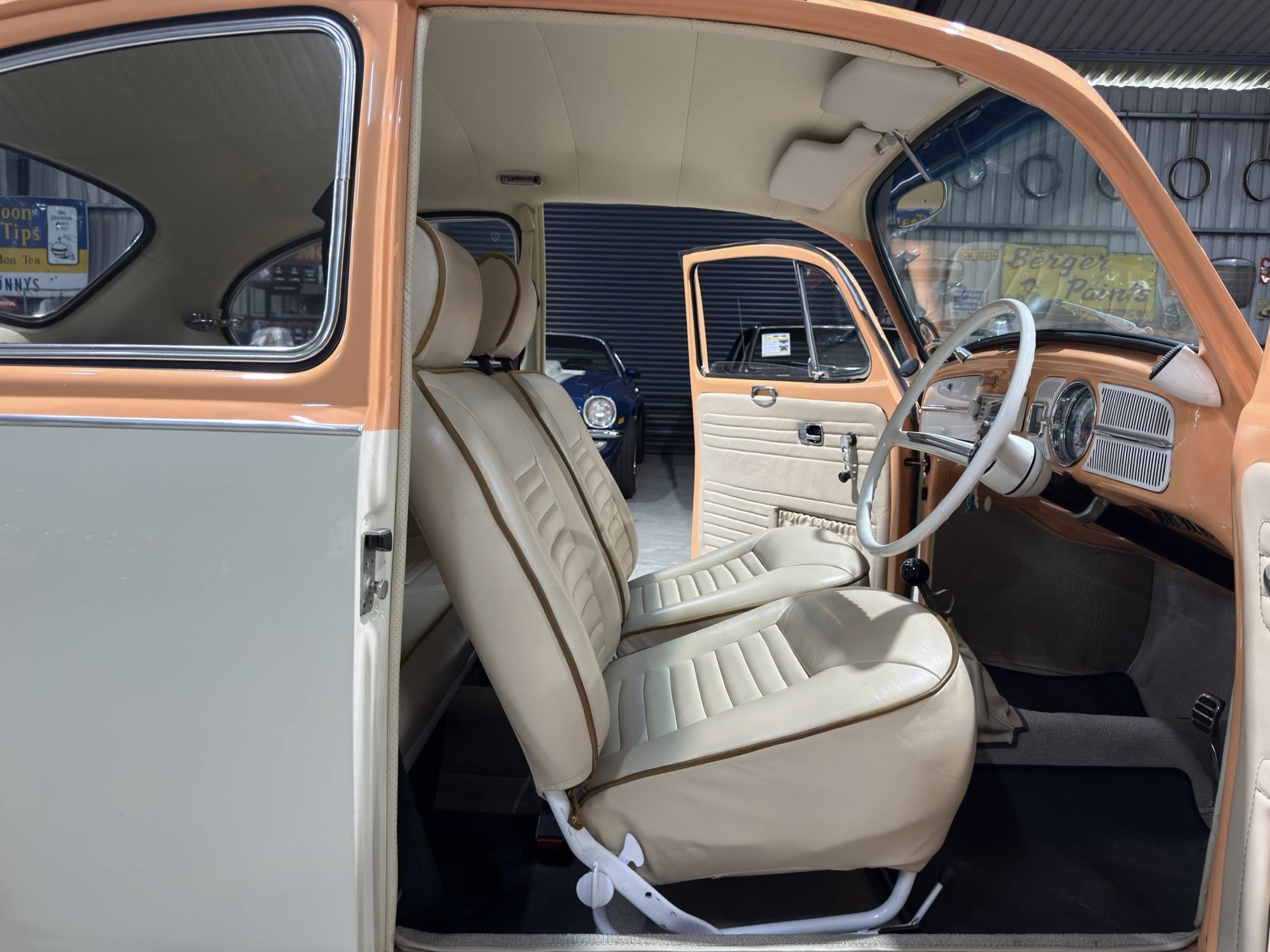 Interior of a vintage orange and beige car, showing front seats, dashboard, and steering wheel with the door open.