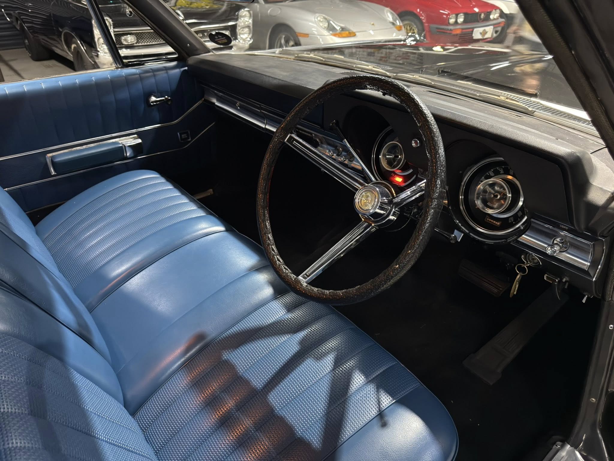 Interior of a vintage car with blue pleated seats, chrome trim, and a dark dashboard visible from the passenger side