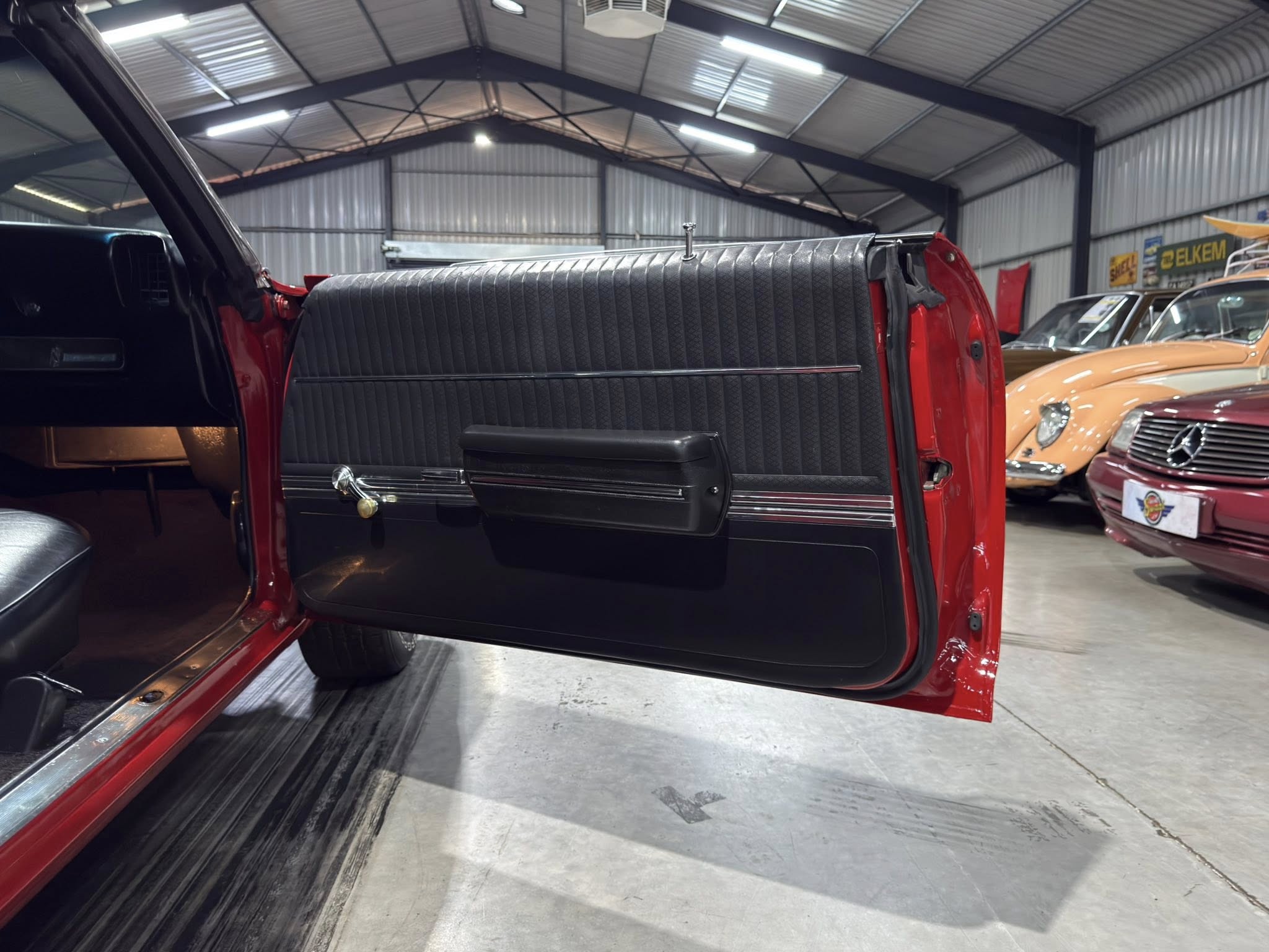 Open red vintage car door with black interior panel, chrome trim, inside a classic car showroom.