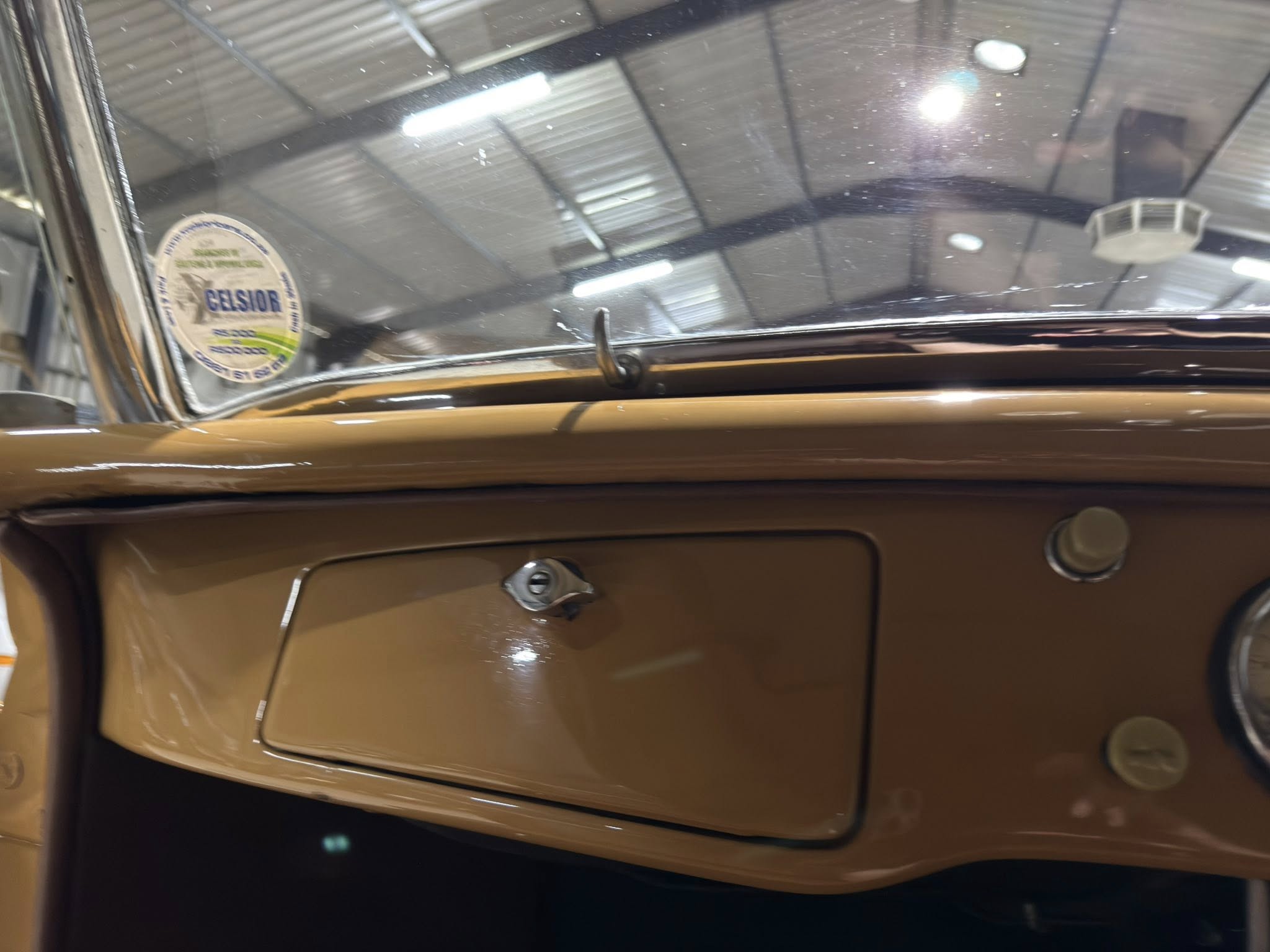 Close-up of a vintage car interior in brown/beige, showing a circular window sticker on the left side inside the door.