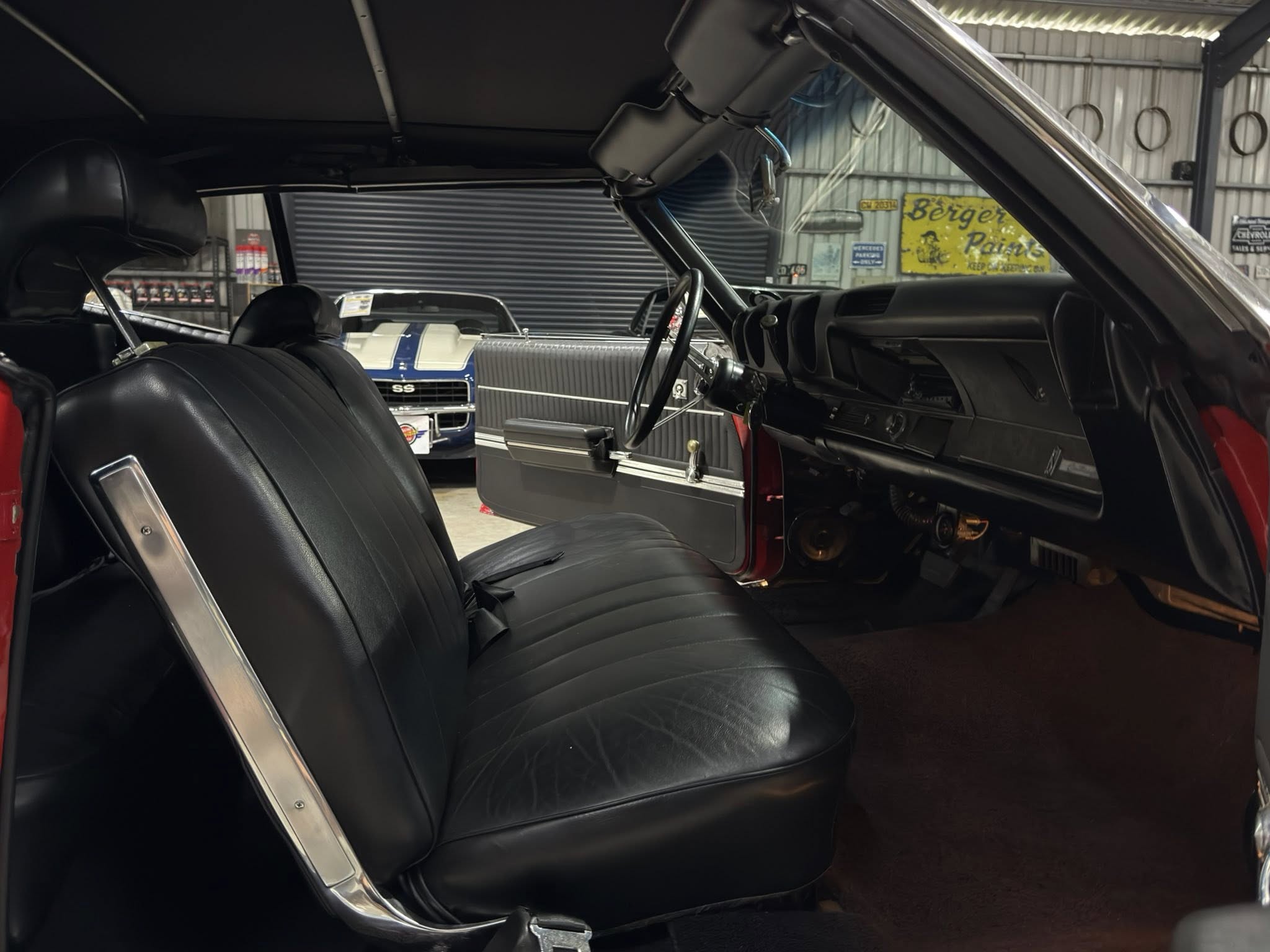Interior of a vintage black car with leather seats and a classic steering wheel in a garage setting.