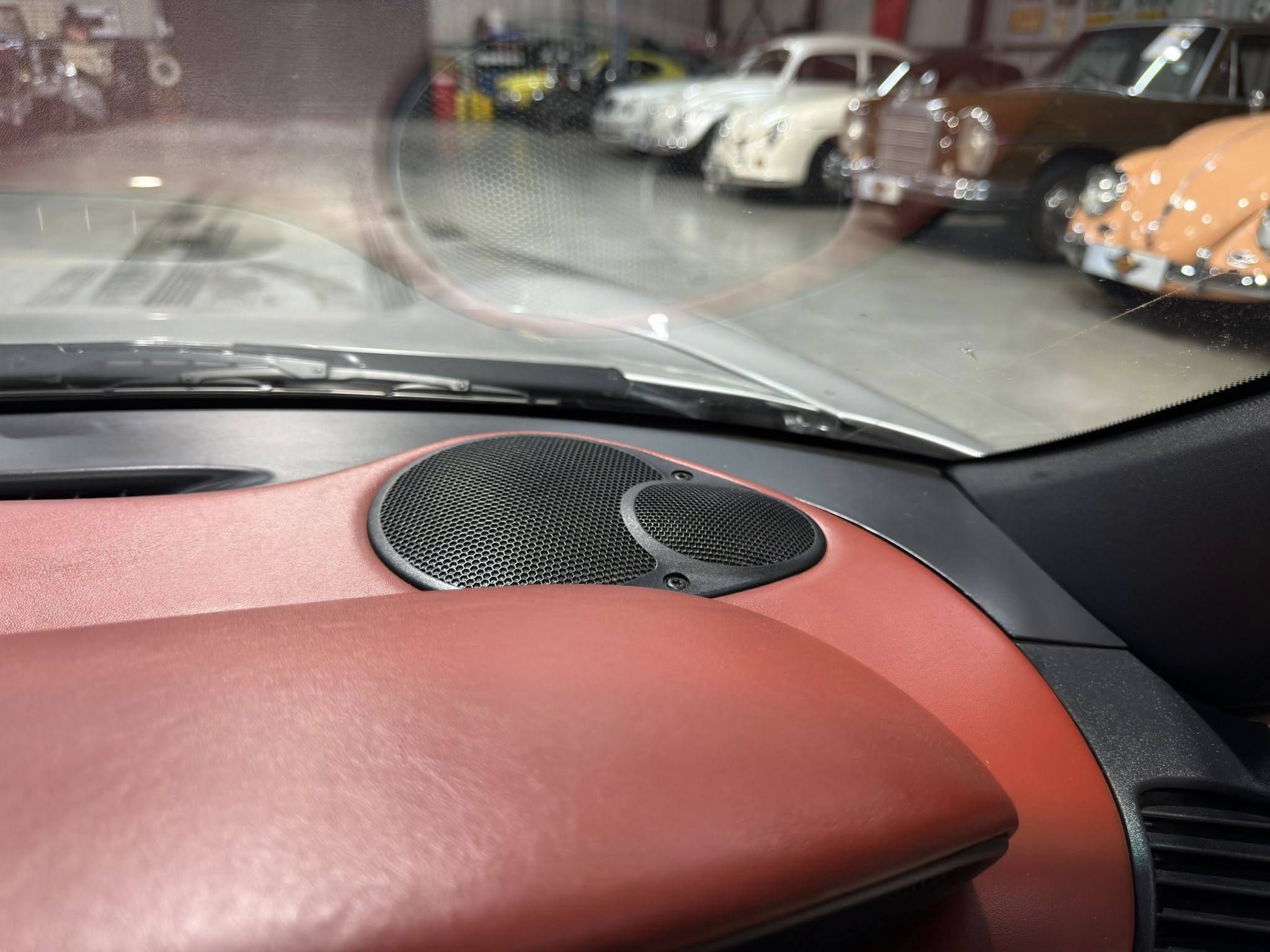 View from inside a car showing a showroom with vintage cars through the windshield, blurred by the glass and reflections.
