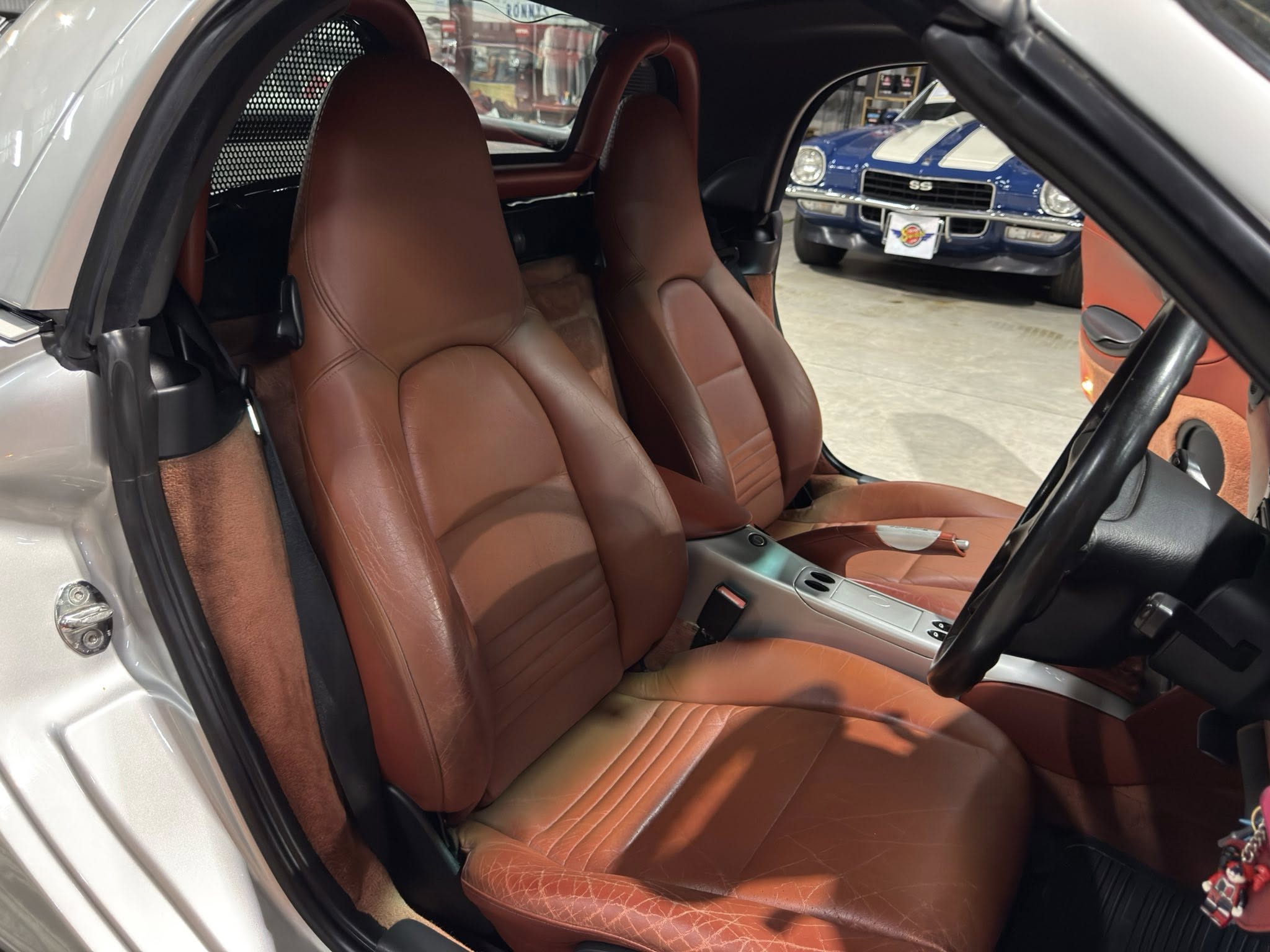 Brown leather front seats in a two-seater car, with a blue classic car visible outside the window.