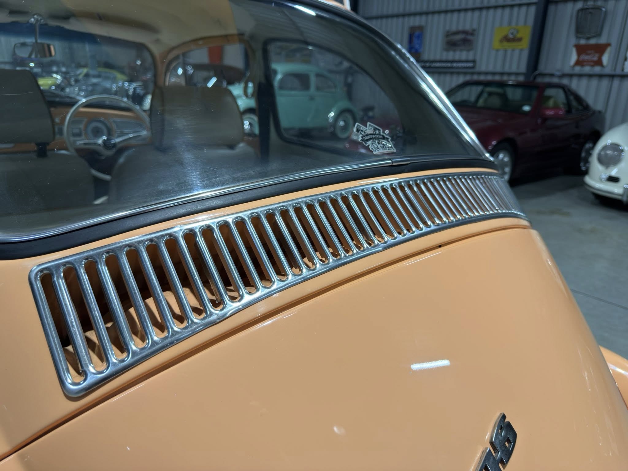Close-up of an orange vintage car front with chrome vertical grill and curved windshield, showroom of classic cars in the background