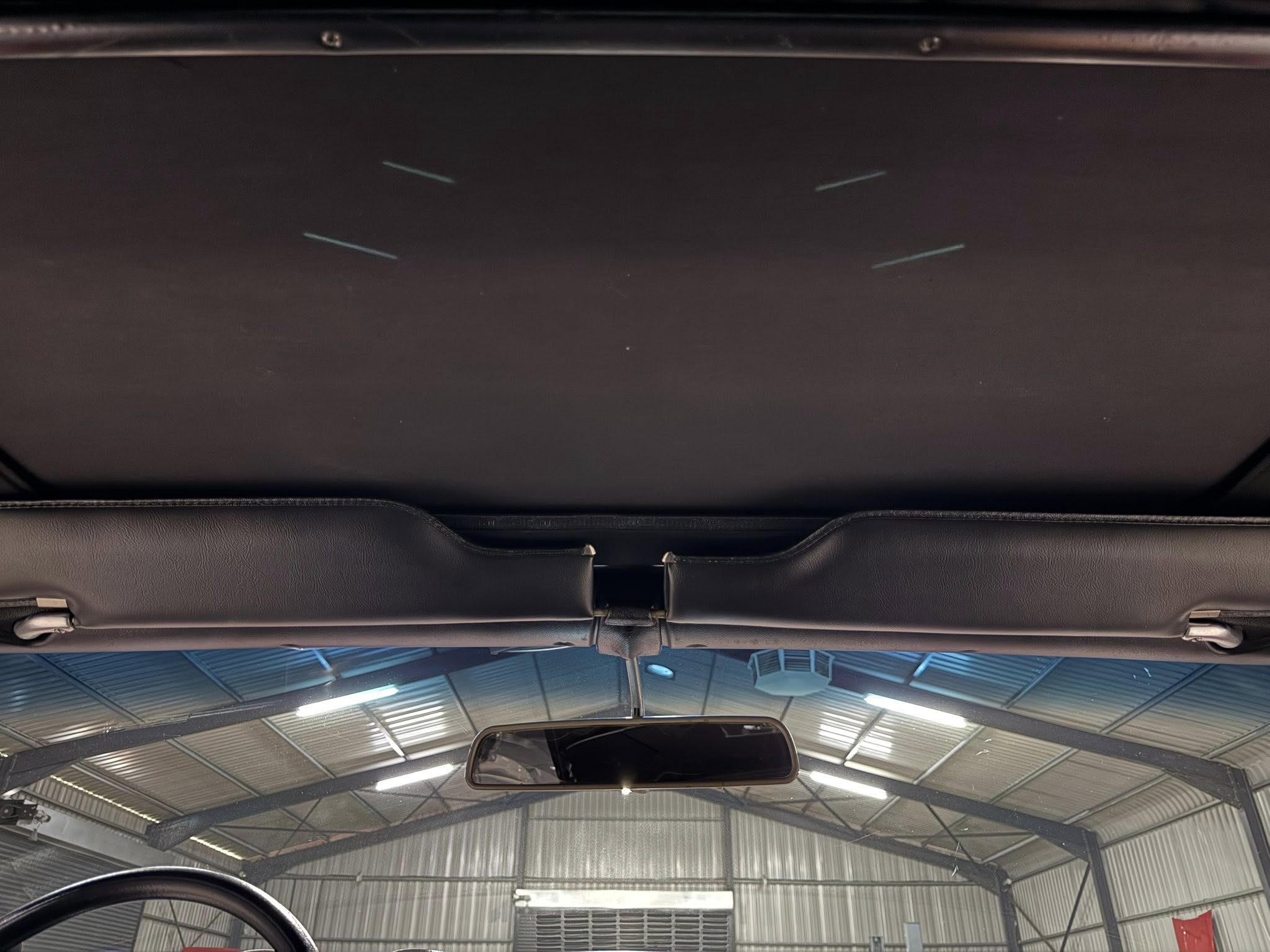 Interior of a car viewed from the driver’s seat, looking up at the headliner, sun visors, and rearview mirror inside a garage.