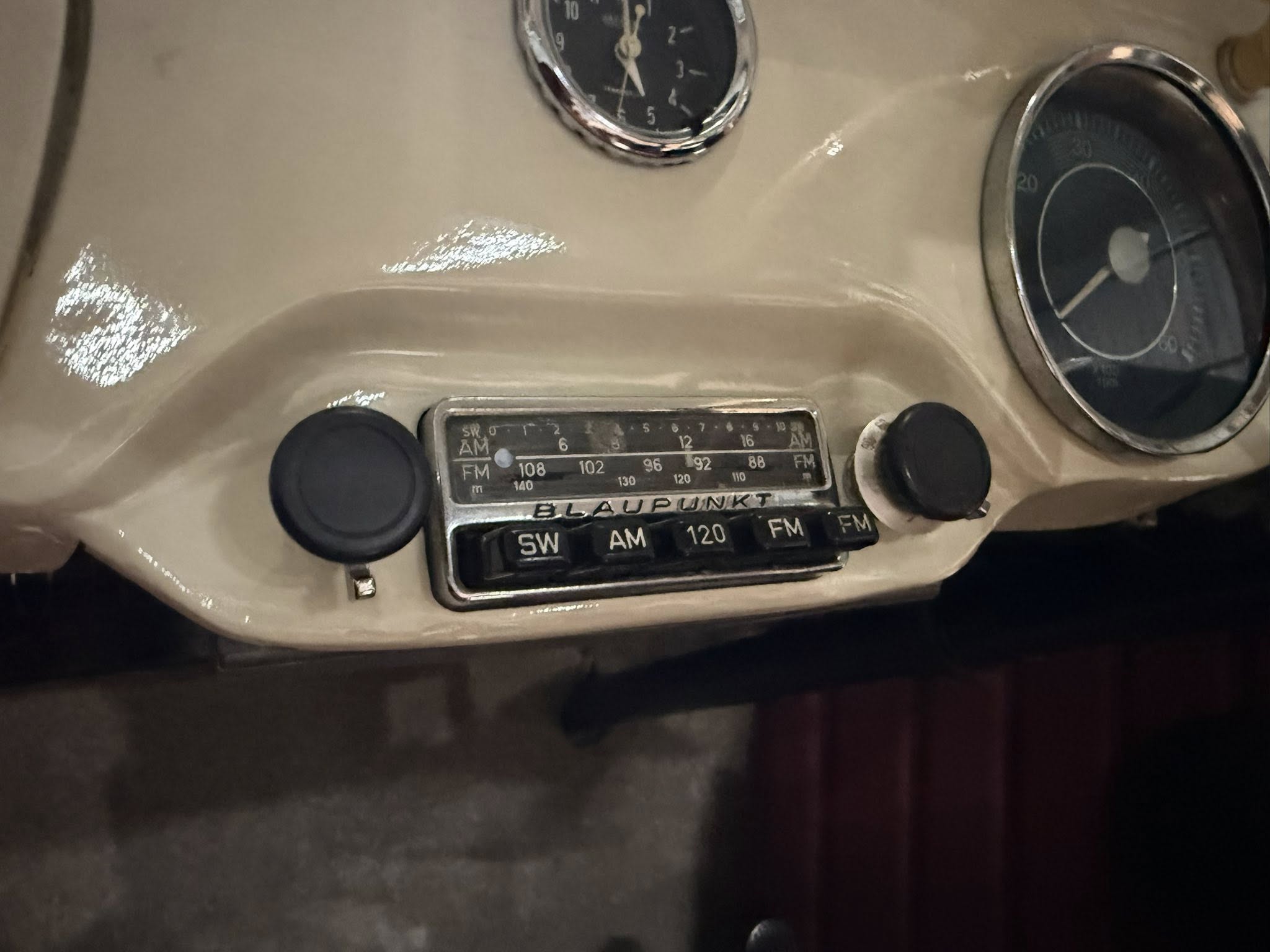 Beige vintage car dashboard showing a Blaupunkt AM/FM radio between two round gauges: a clock on the left and a speedometer on the right.