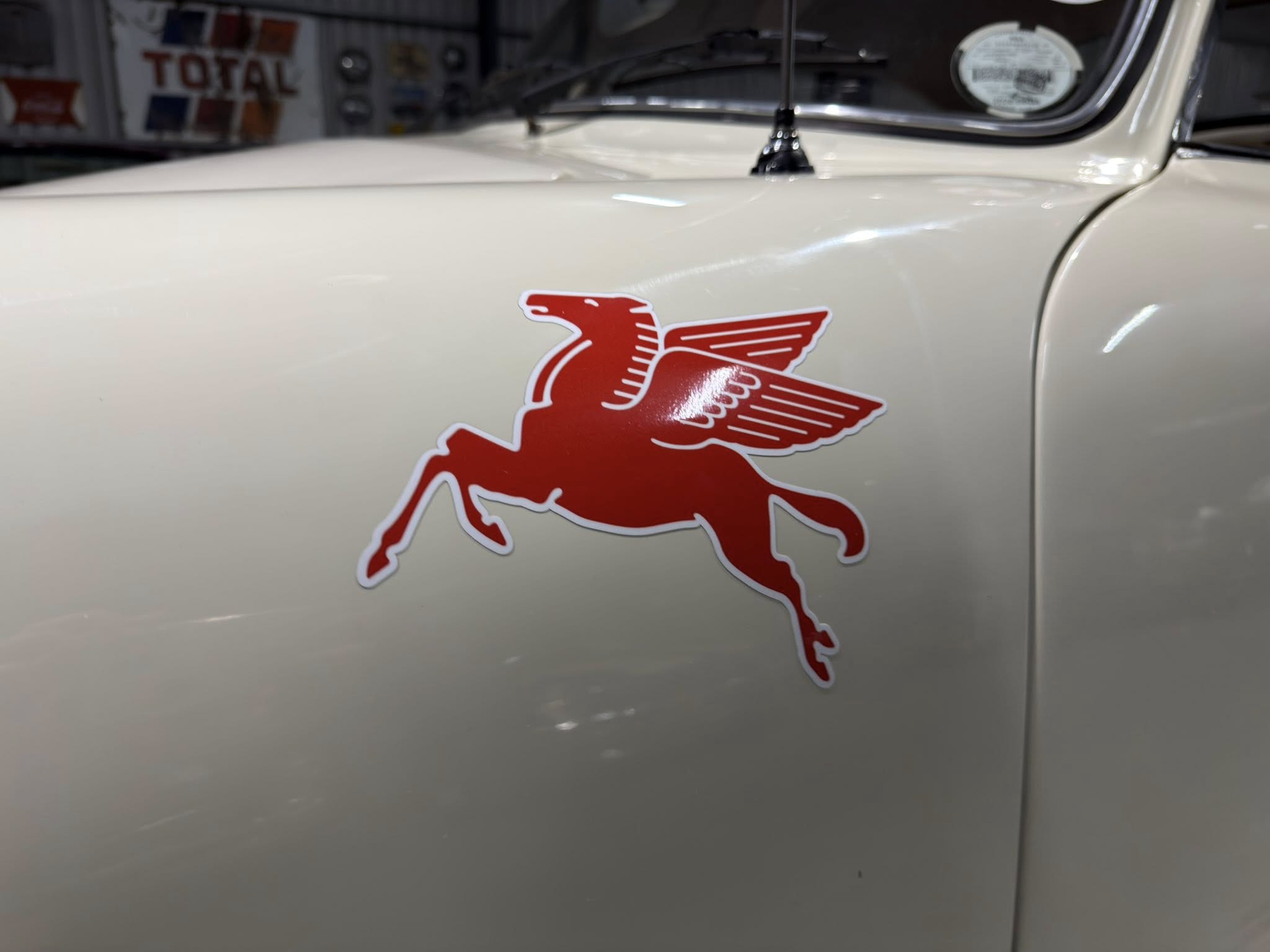 Close-up of a red Mustang horse decal on a light-colored vintage car door, with the windshield visible in the background.